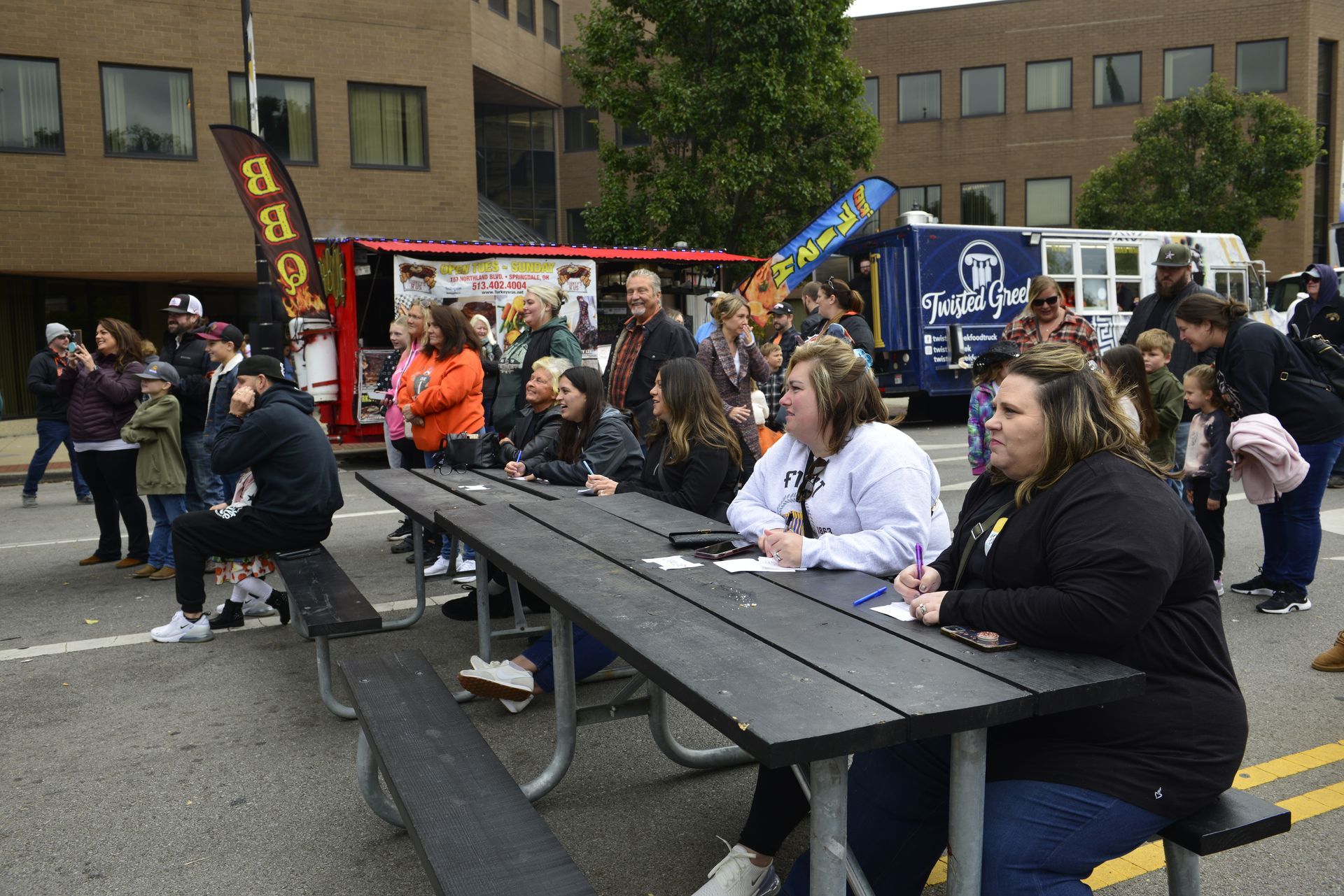 a group of people are sitting at picnic tables on the side of the road