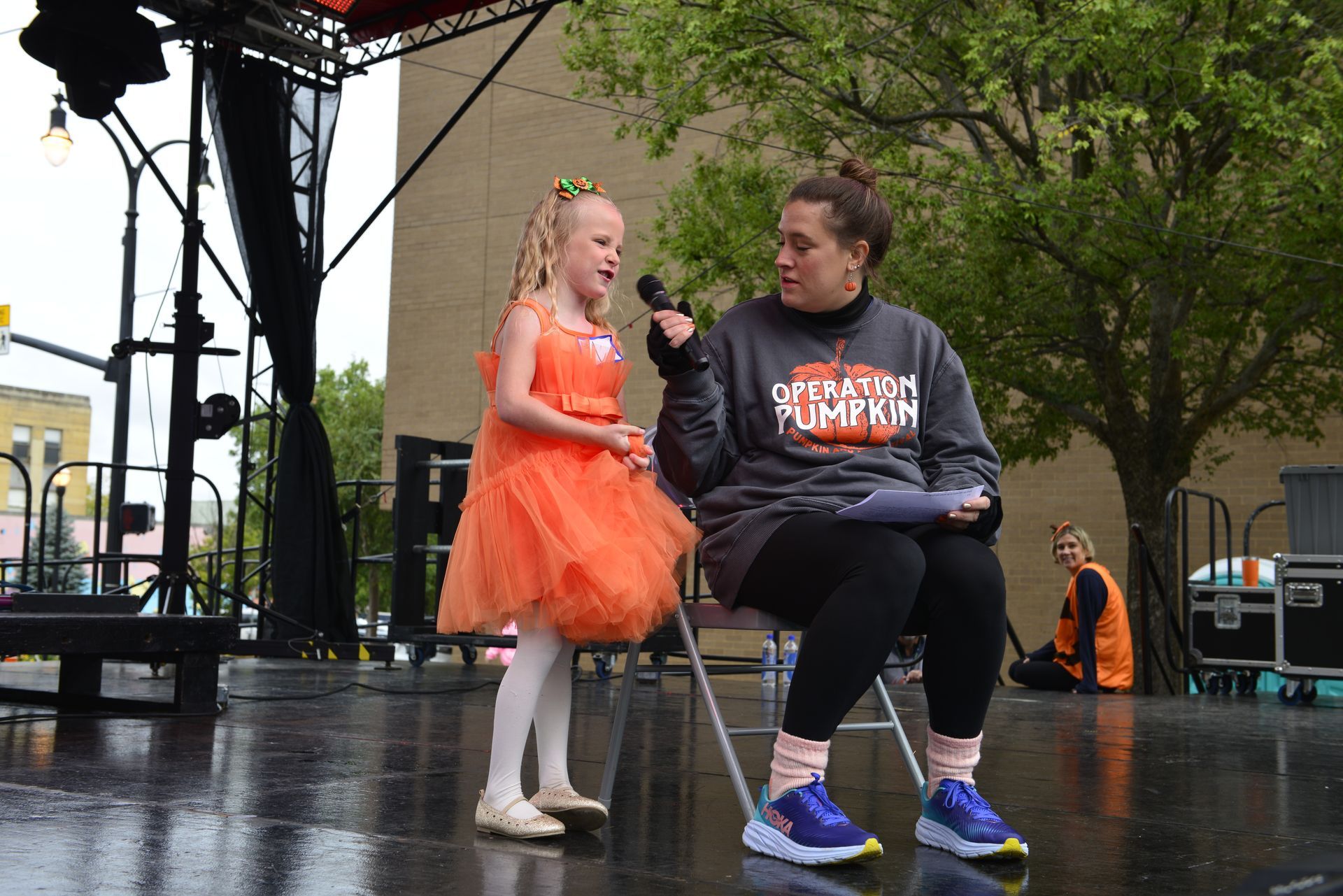 a woman is sitting in a chair while a little girl sings into a microphone