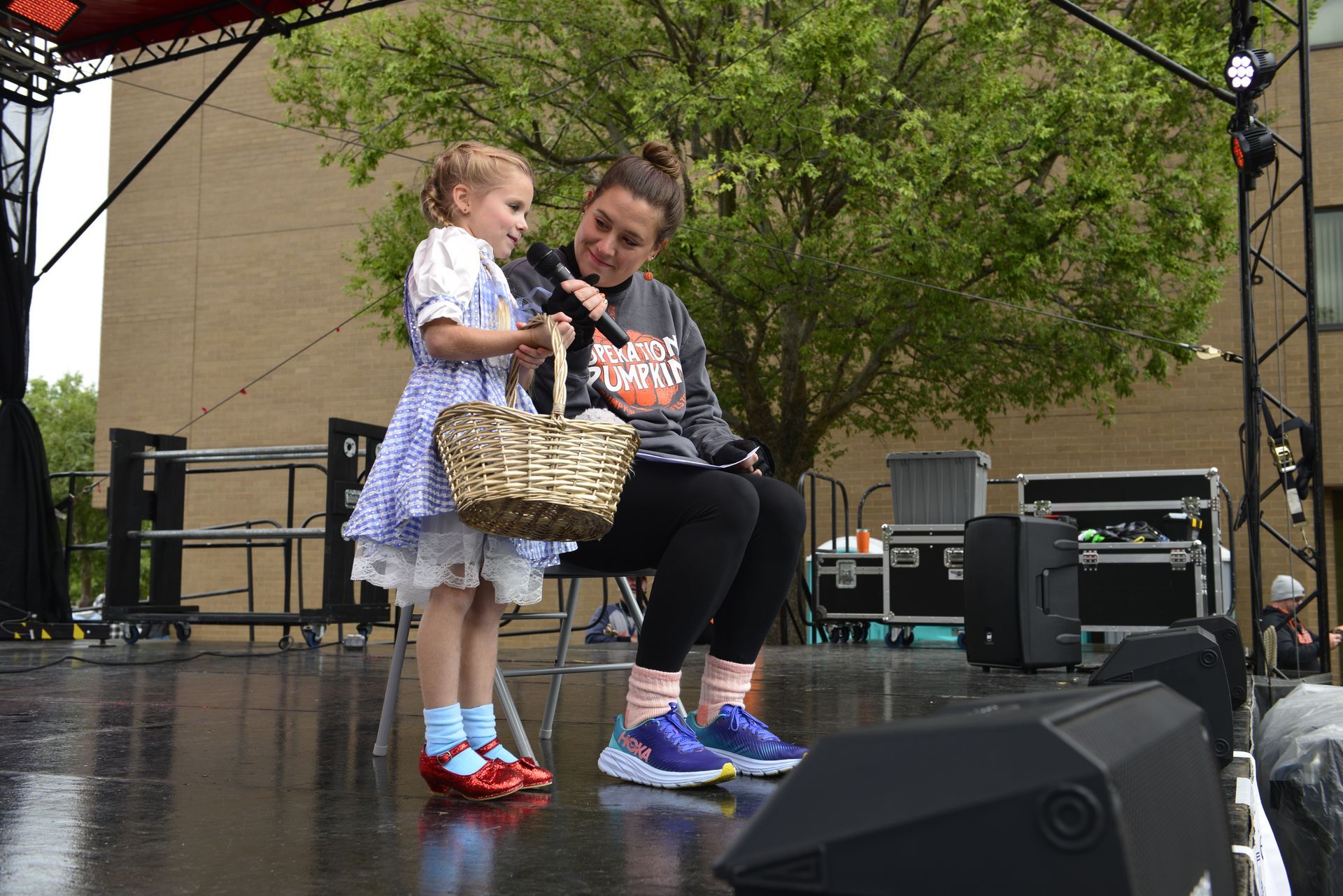a little girl is sitting next to a woman on a stage holding a microphone