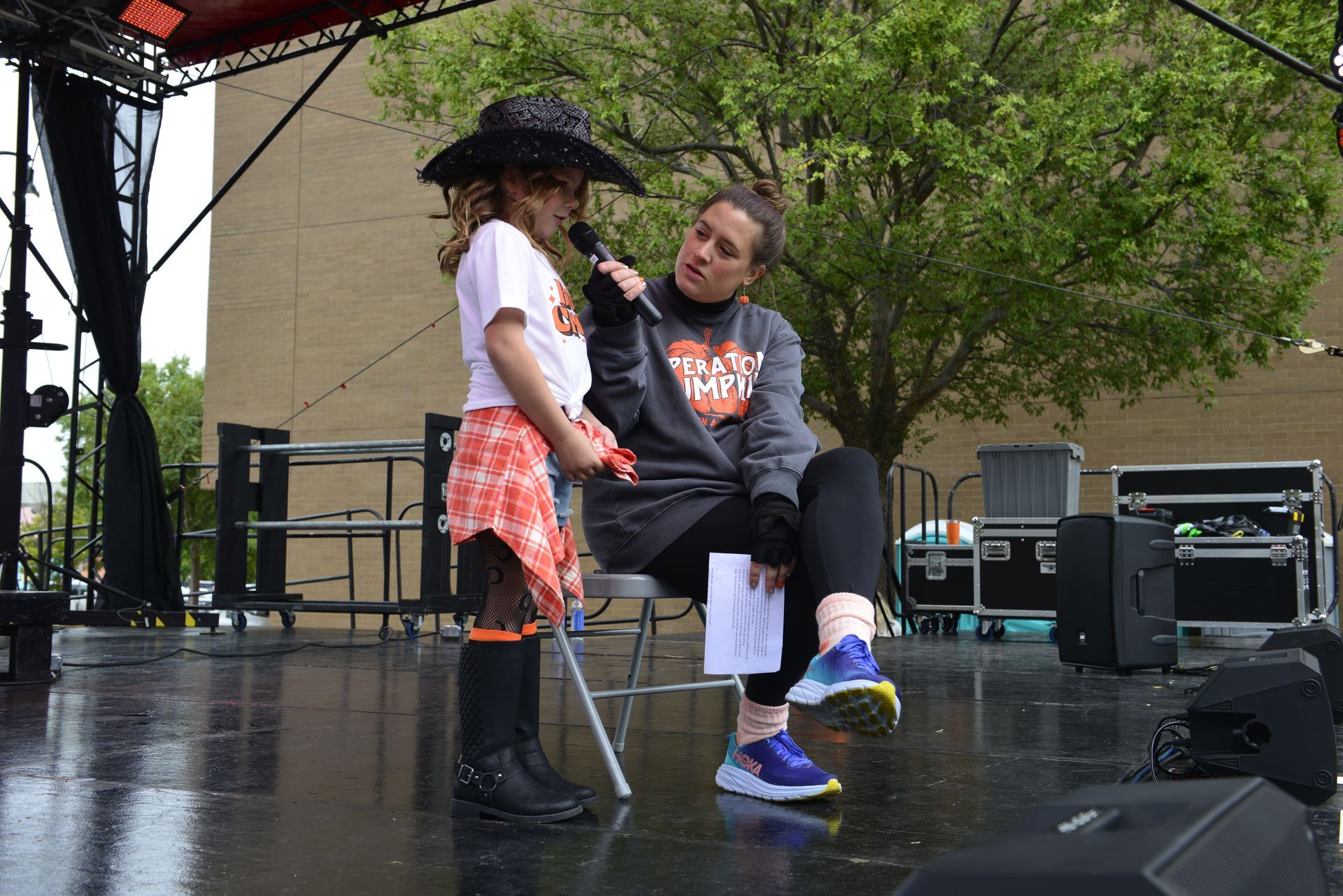 a woman is sitting on a stage talking to a little girl who is wearing a witch costume