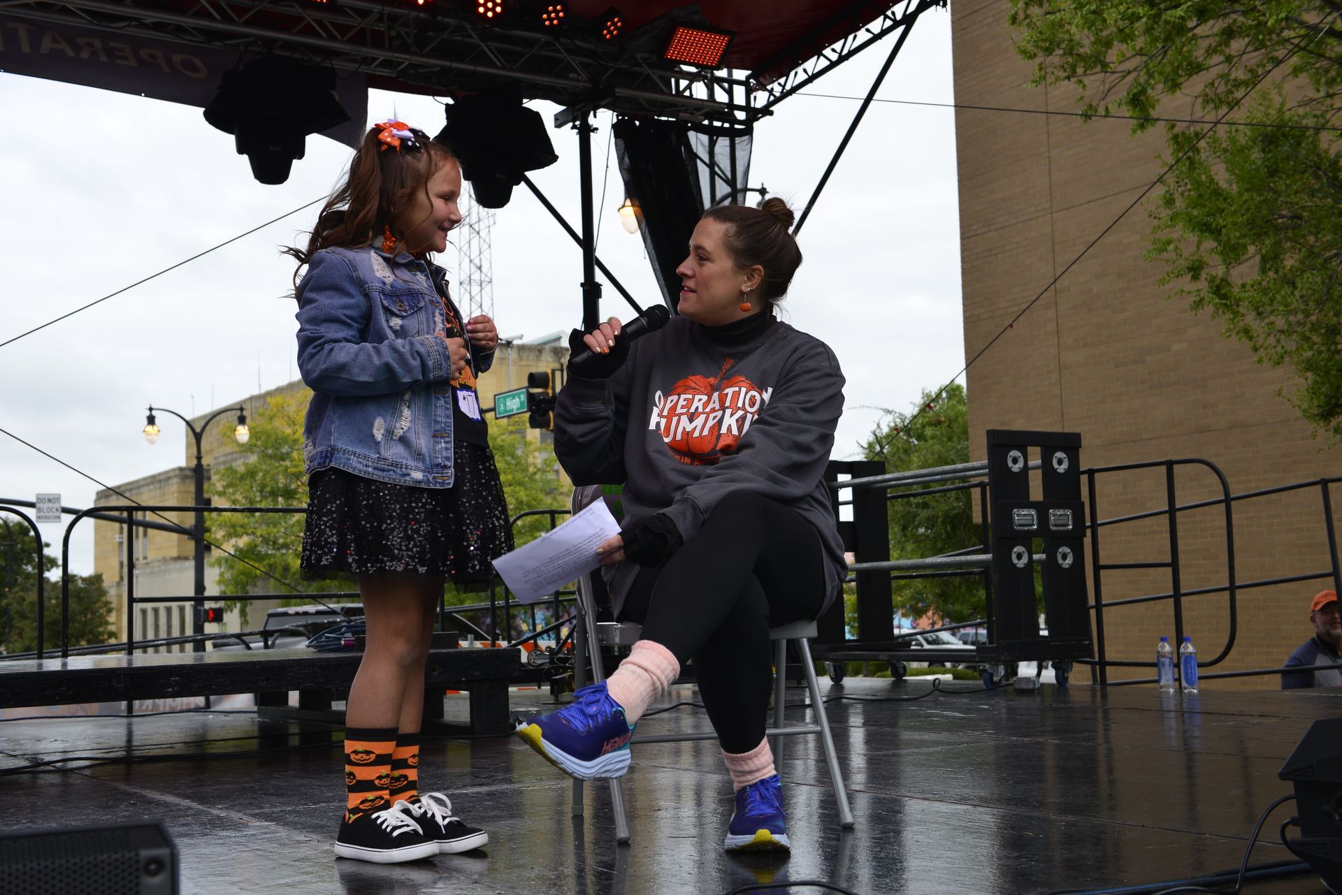 a woman is sitting on a stool talking to a little girl on a stage