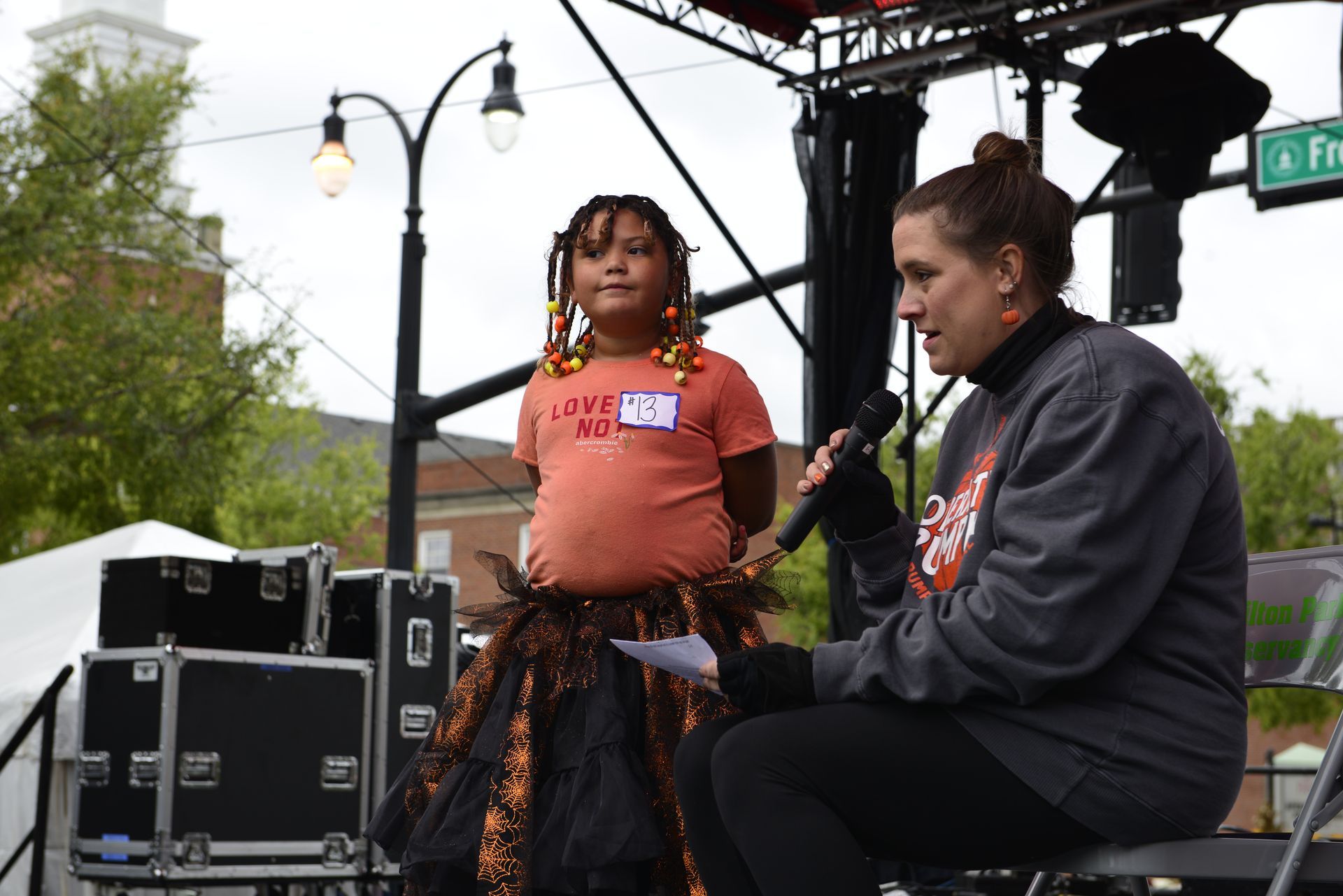 a woman is sitting on a chair talking into a microphone while another woman stands behind her