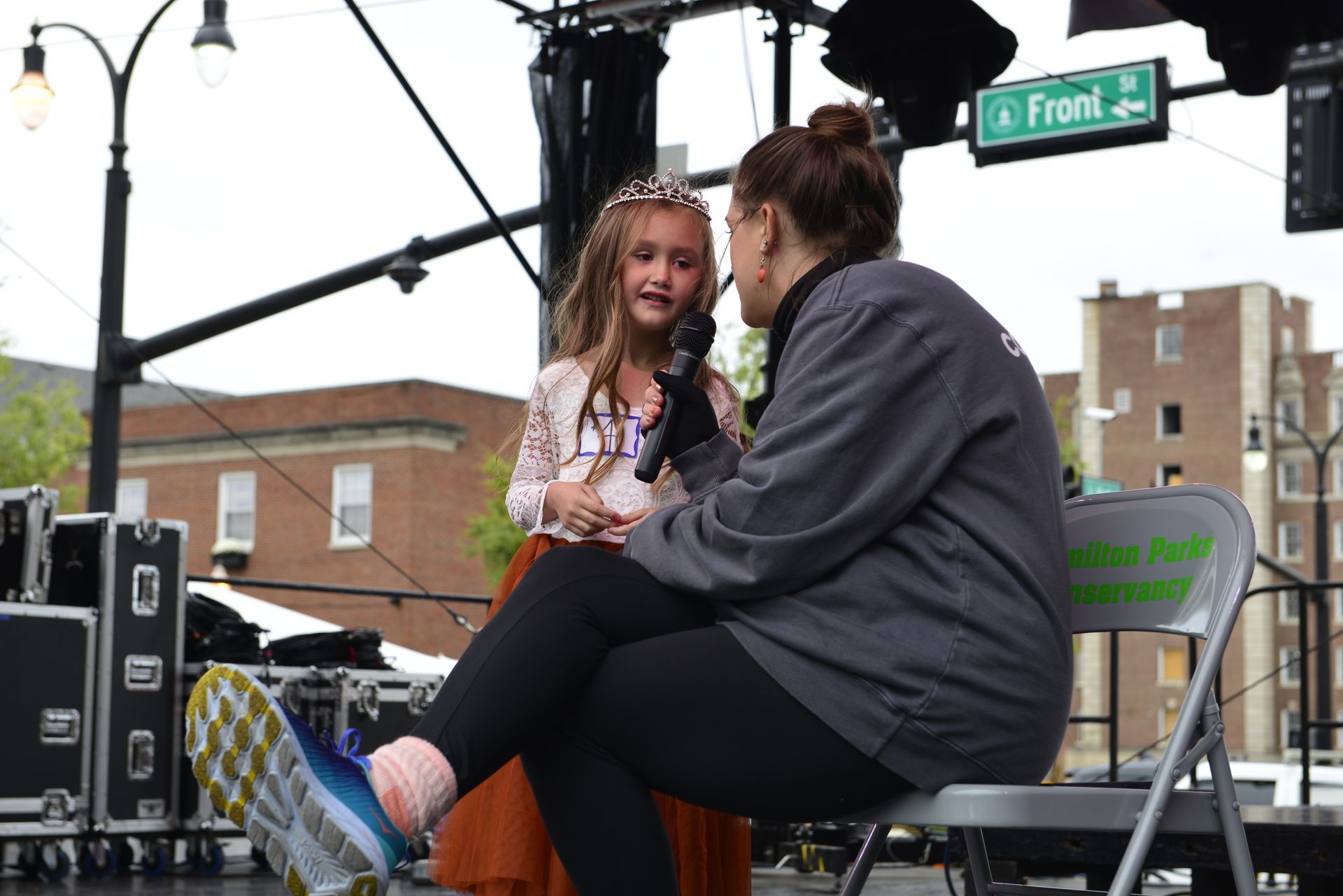 a woman is sitting on a chair talking to a little girl with a microphone