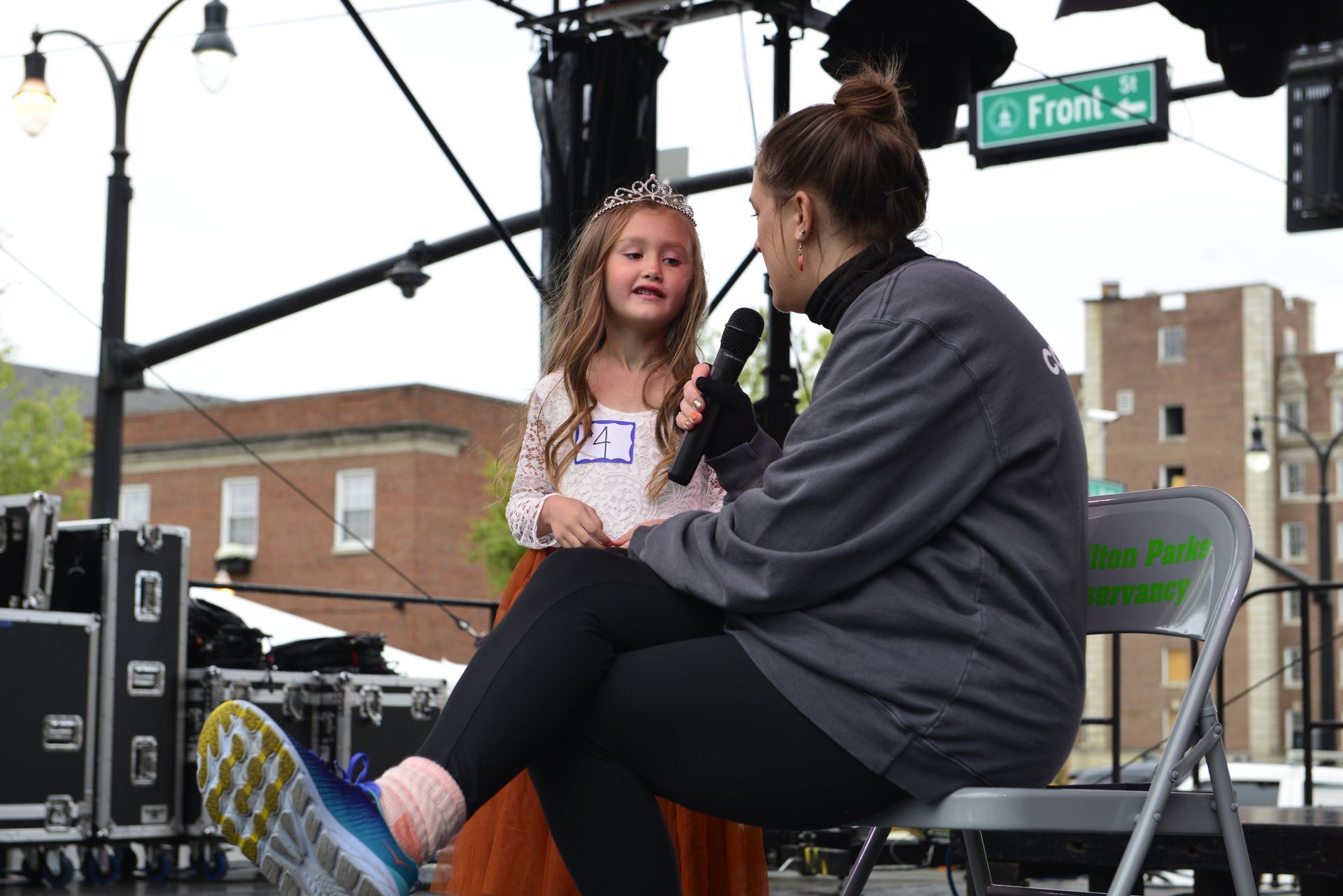 a woman is sitting in a chair talking to a little girl with a microphone