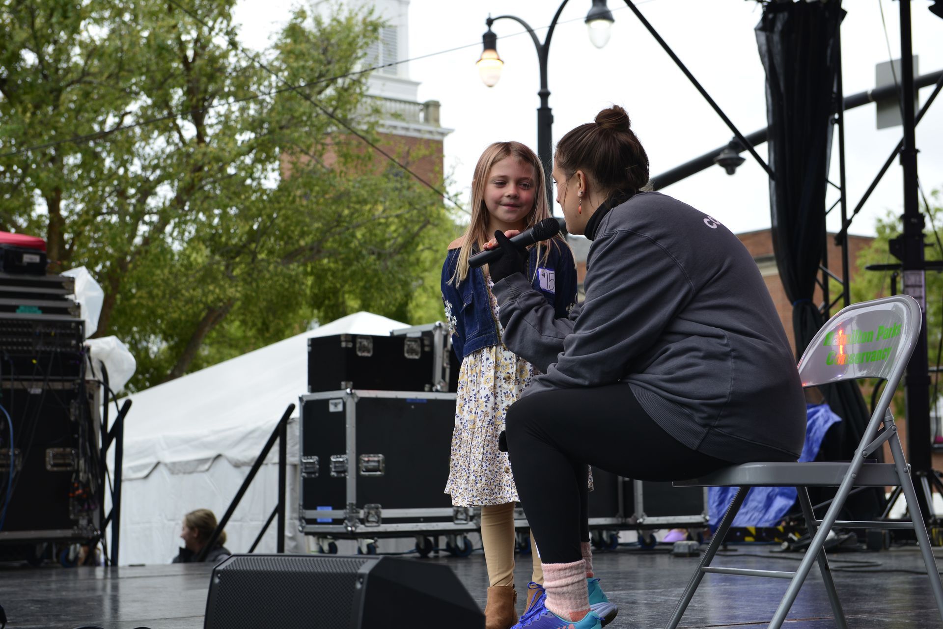 a woman is sitting on a chair talking to a little girl on a stage