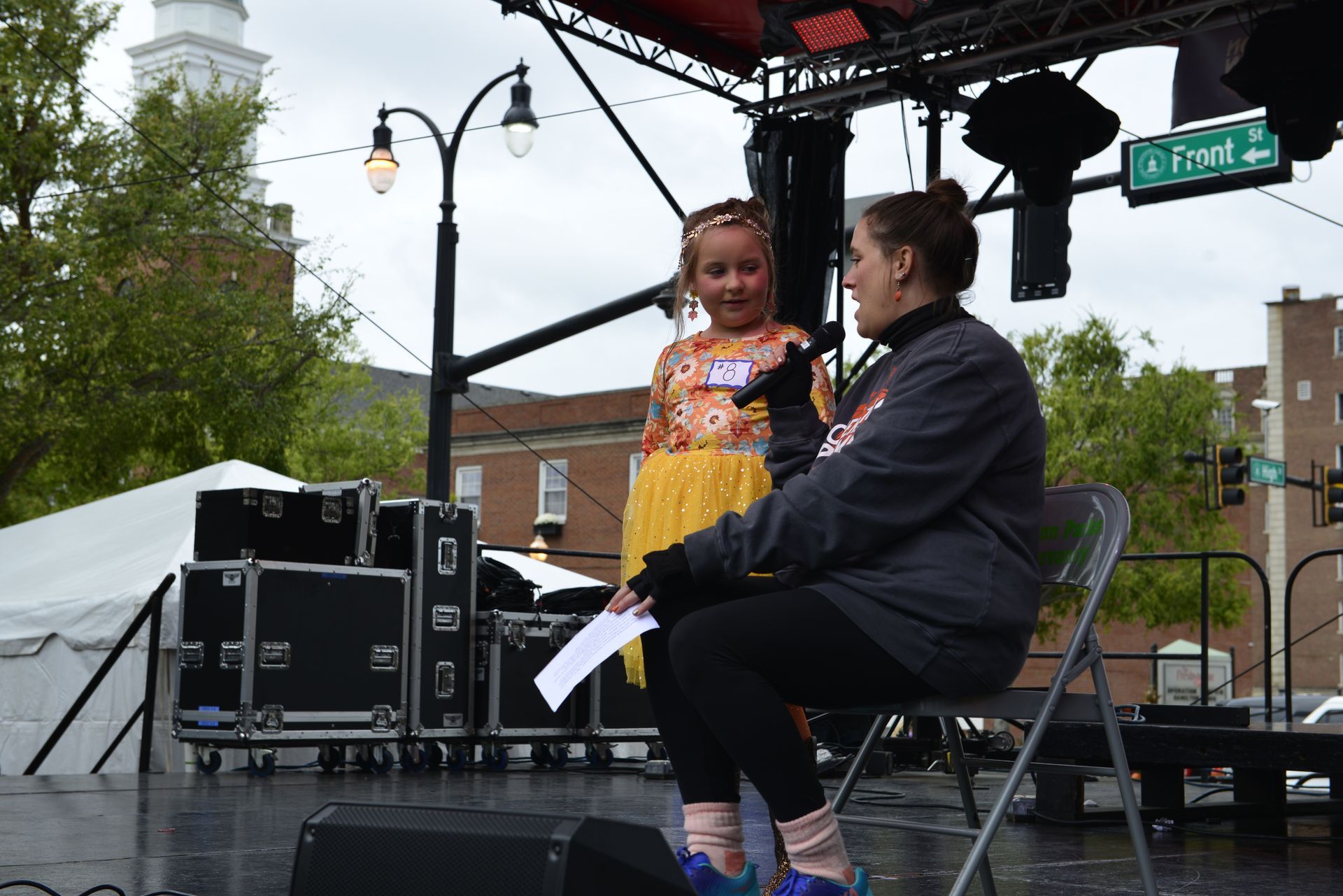 a woman is sitting on a stage talking to a little girl