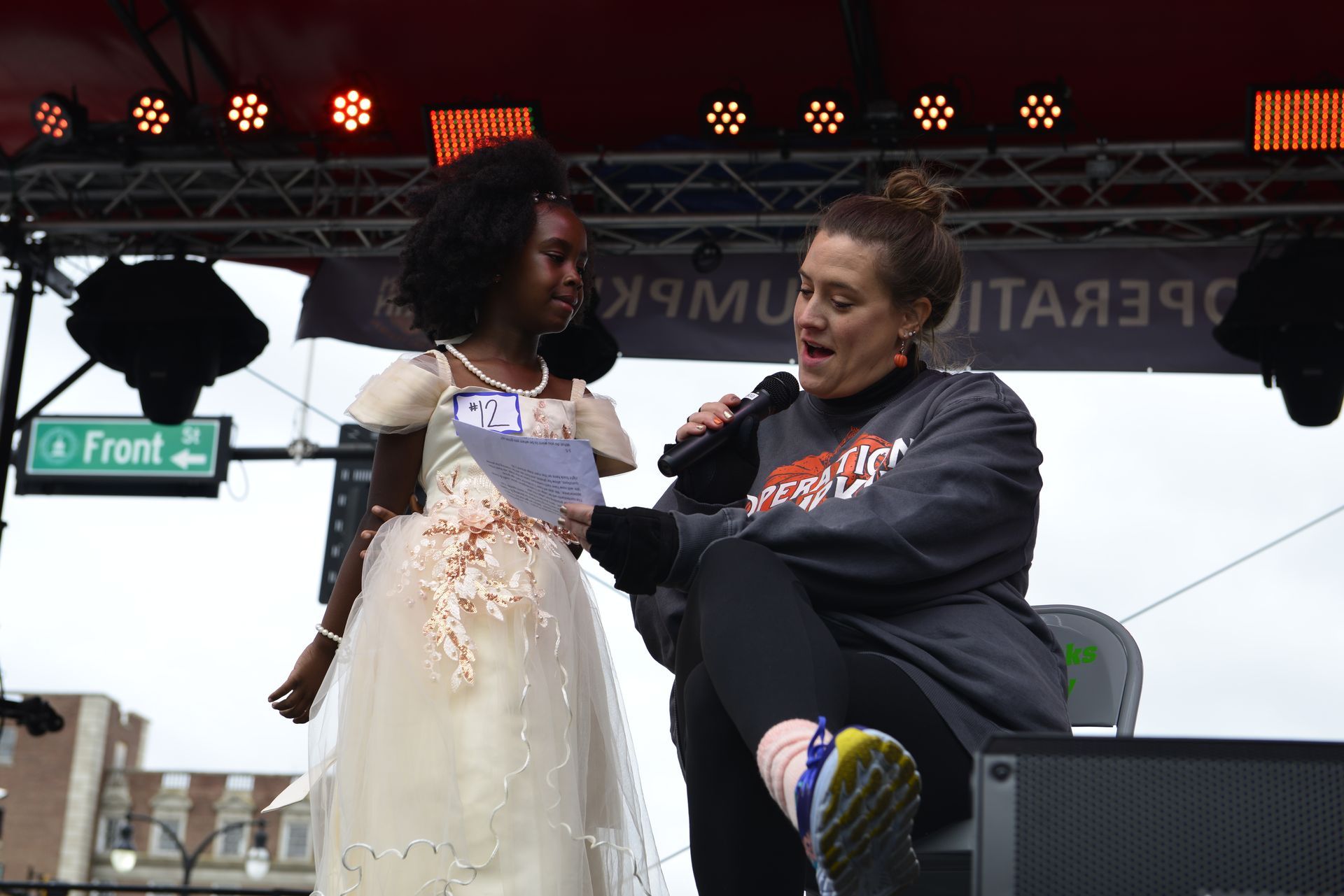 a woman is speaking into a microphone next to a little girl in a white dress