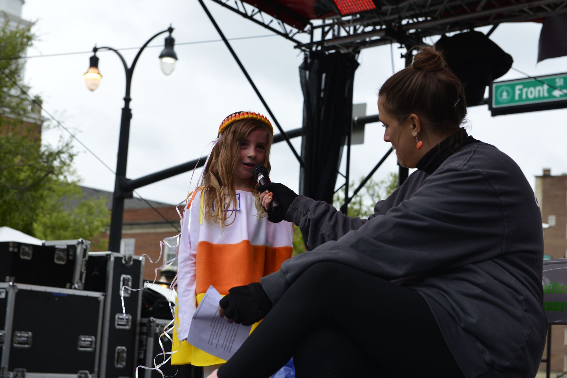 a girl in a candy corn costume is being interviewed by a woman in front of a street sign that says front