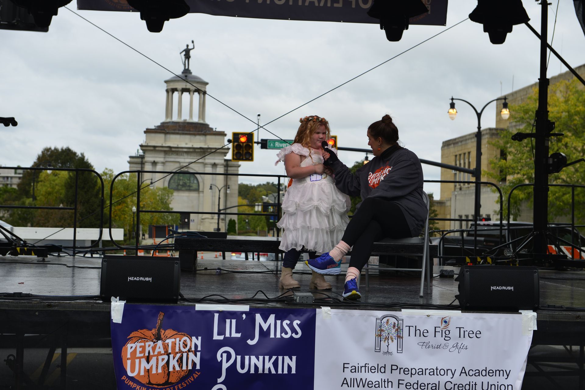 a little girl in a white dress is being held by a woman on a stage