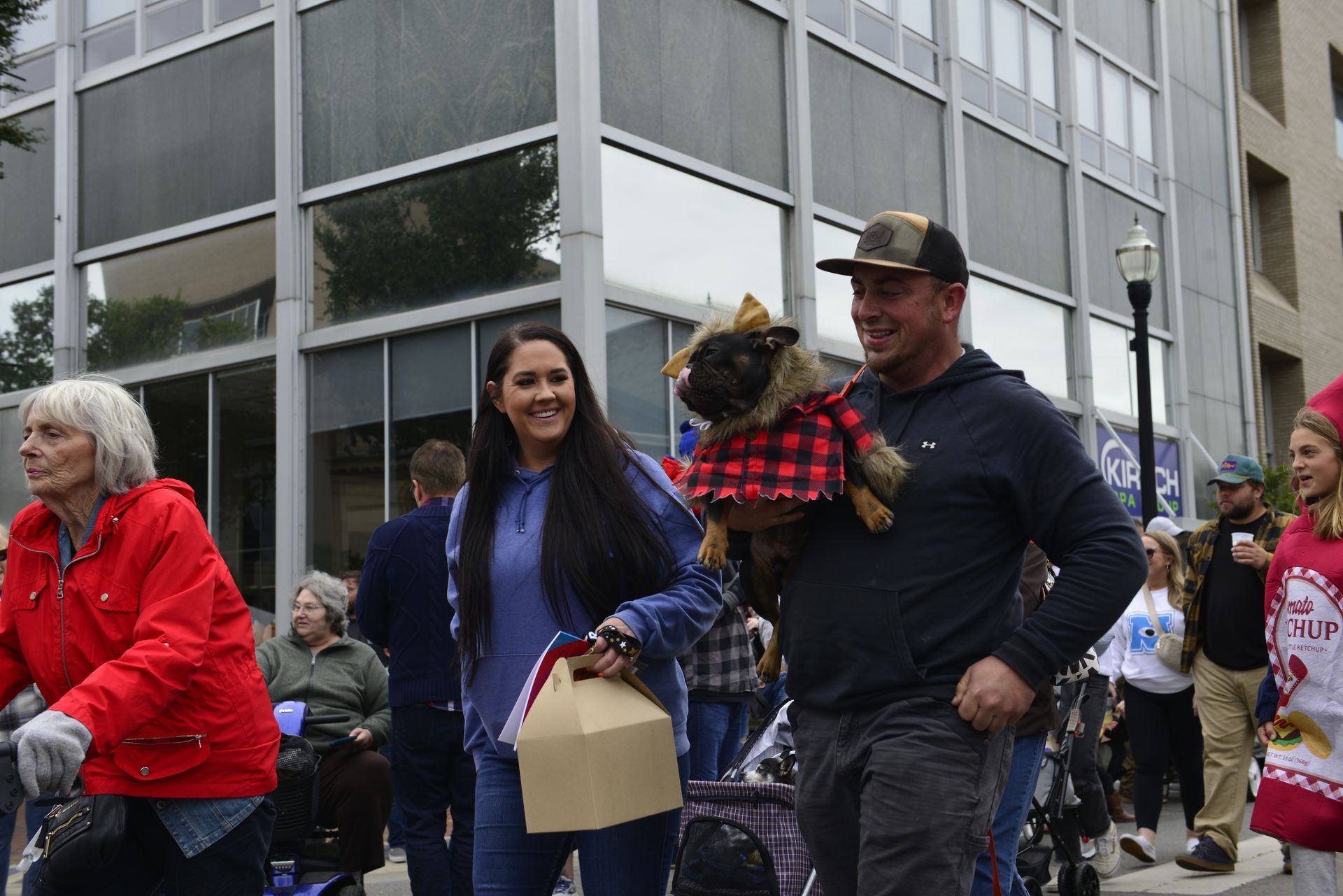 a group of people are walking down a street with a dog in a stroller