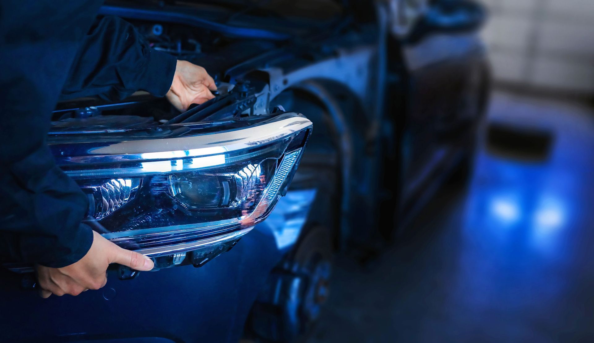 Mechanic removing a car headlight; blue-toned setting.