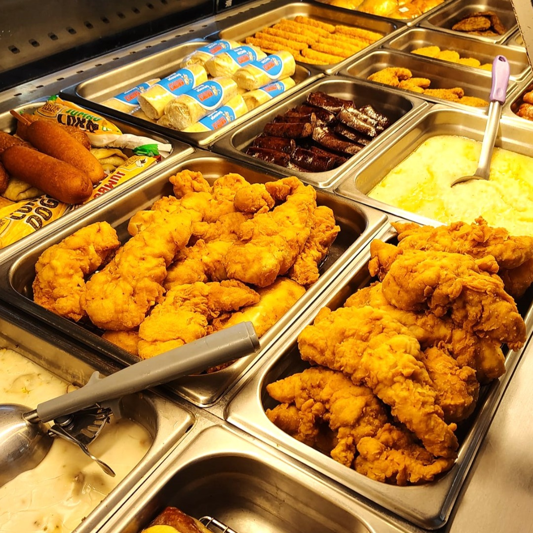 Buffet with trays of fried chicken, corn dogs, mashed potatoes, and other hot foods.