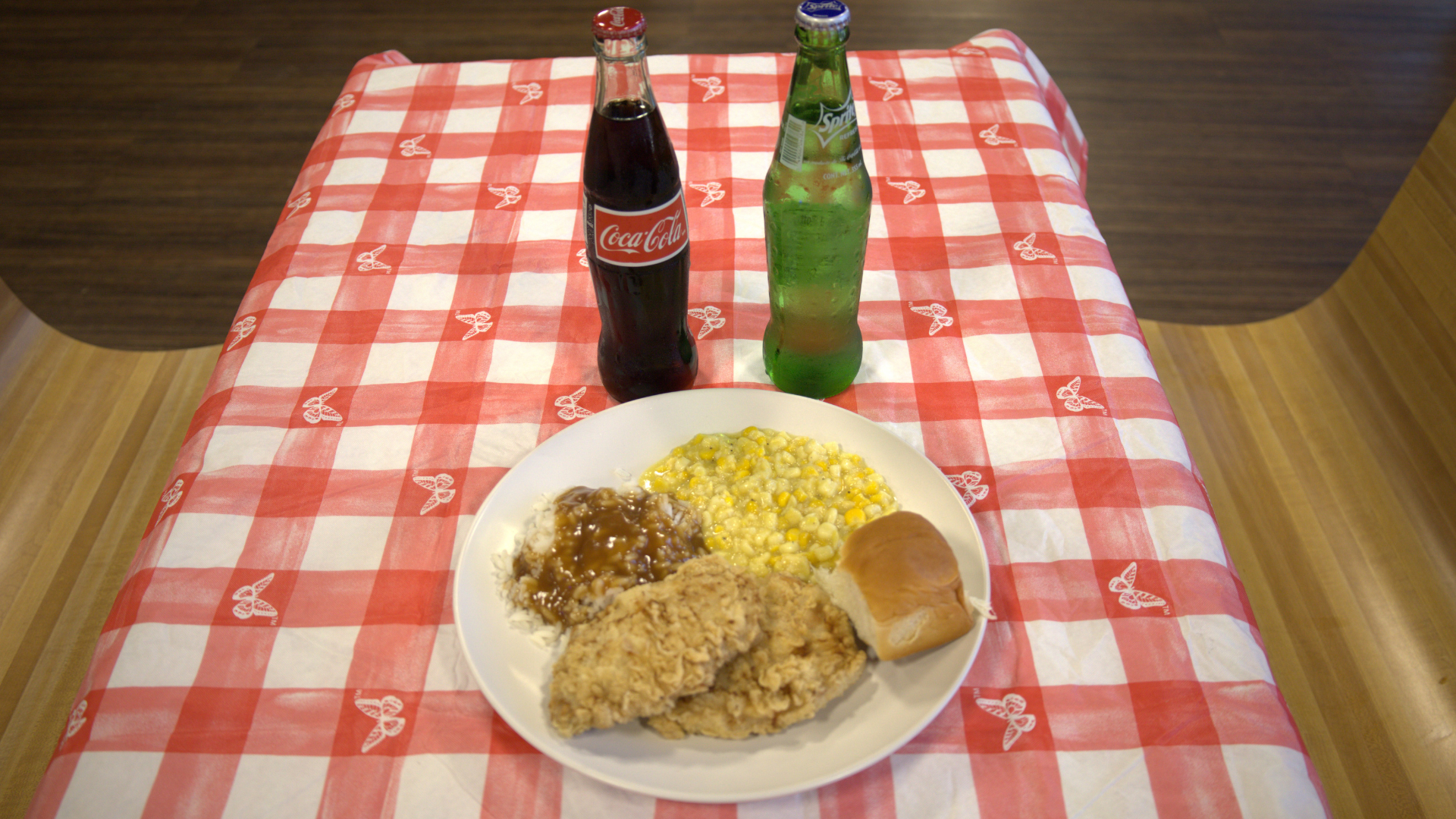 Coca-Cola bottle and green soda bottle behind a plate of rice and side dishes on a red checkered tablecloth
