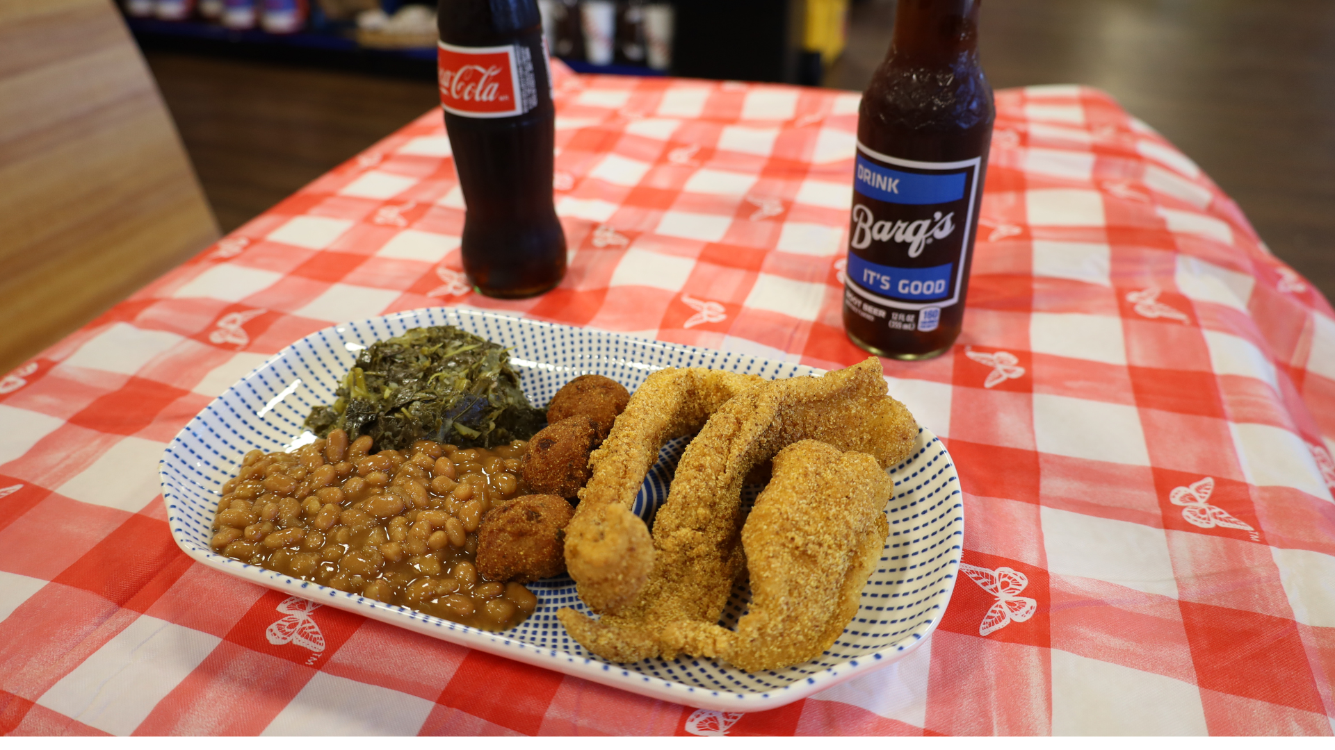 Fried food platter with rice, greens, and two Coke bottles on a red checkered tablecloth.