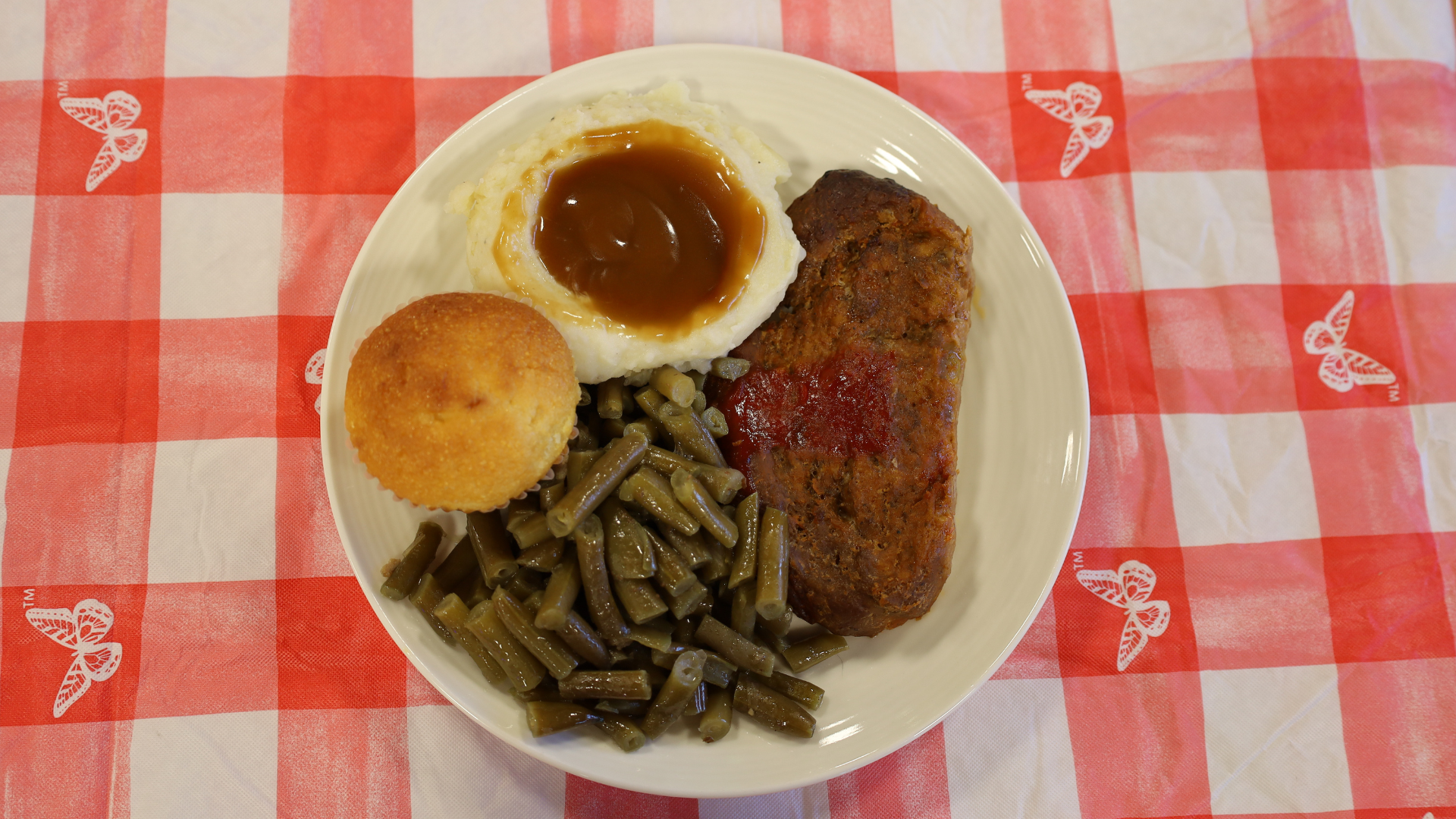 Plate of breakfast: fried egg, hash browns, steak, and sautéed vegetables on a red checkered tablecloth
