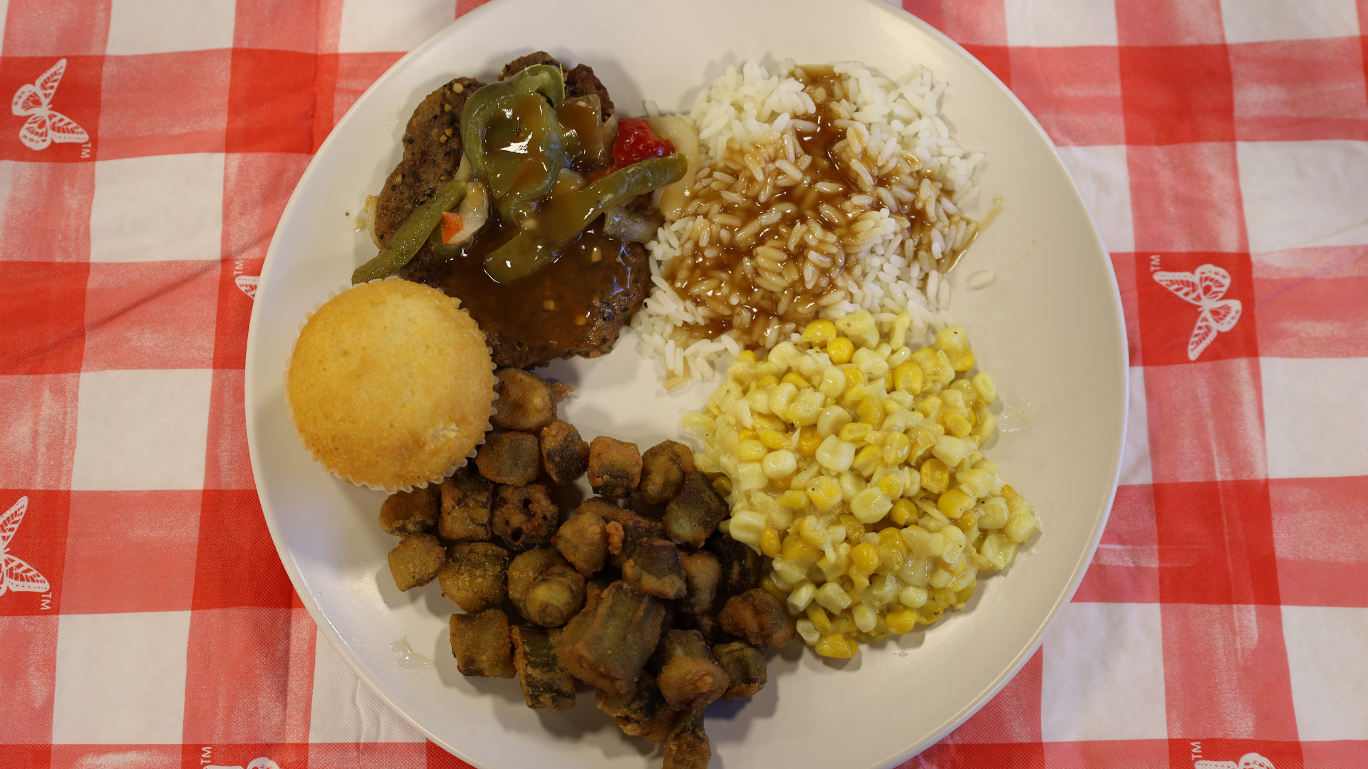 Plate of assorted food on a red checkered tablecloth, with rice, corn, vegetables, fried balls, and meat cubes