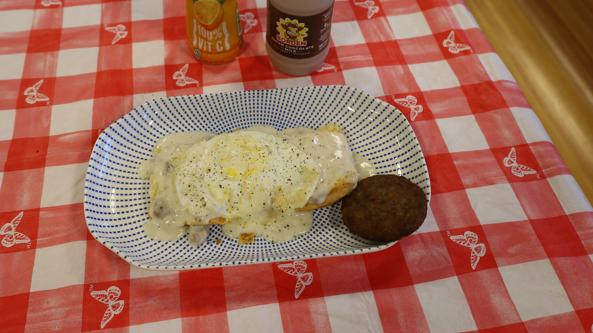 A plate with a cheese-covered omelet and a dark patty on a red checkered tablecloth, with drinks behind it.