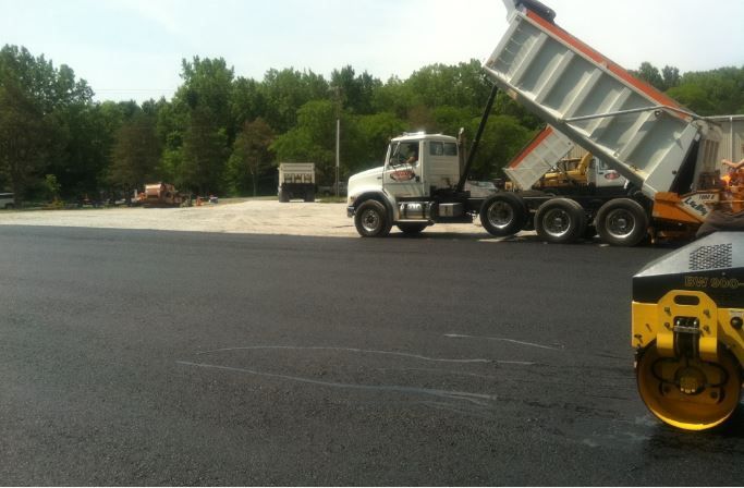 A dump truck is being loaded with asphalt in a parking lot