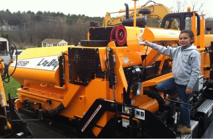 A little girl is standing in front of a large yellow machine that says left