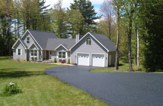 A large house with a driveway leading to it is surrounded by trees.