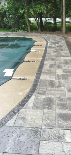 A concrete walkway leading to a swimming pool surrounded by trees.