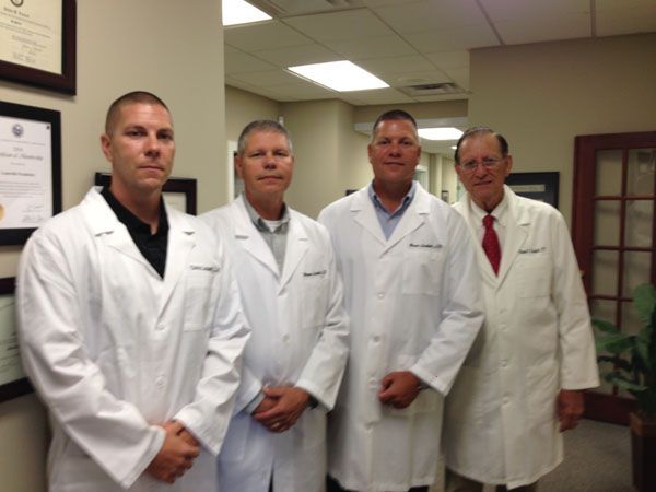 Four people in white lab coats standing in a hallway, likely a medical office.