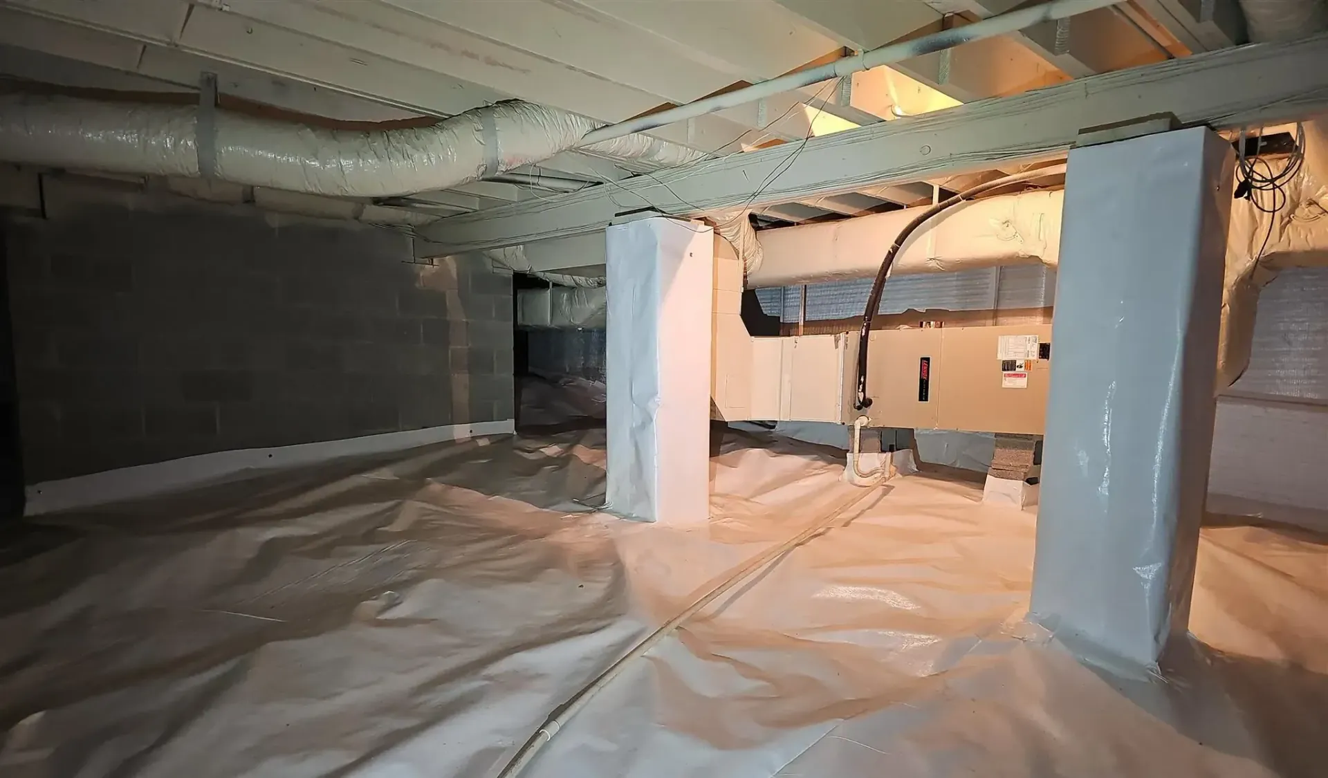 A clean crawl space with white vapor barrier flooring and encapsulated support pillars under a residential home.