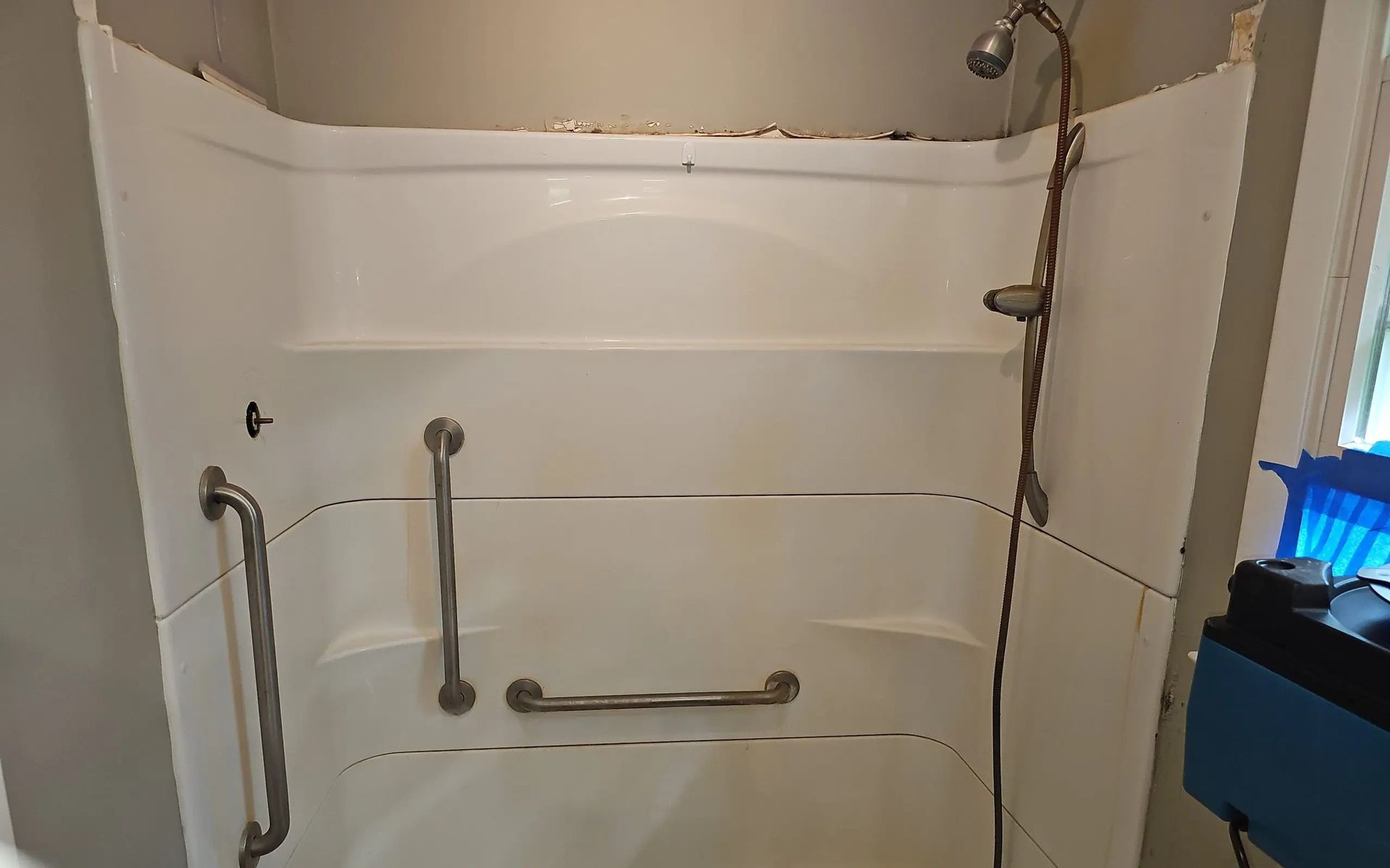 A white shower surround with chrome grab bars installed on the left and center walls, and a handheld shower head on the right.