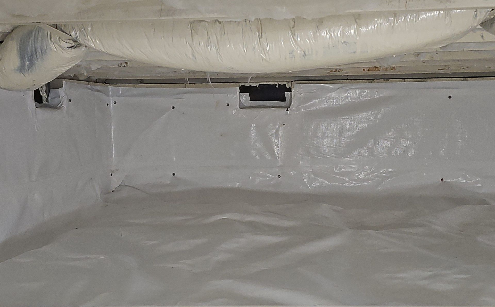 A crawl space encapsulated with white plastic vapor barrier material, with white spray foam insulation overhead.