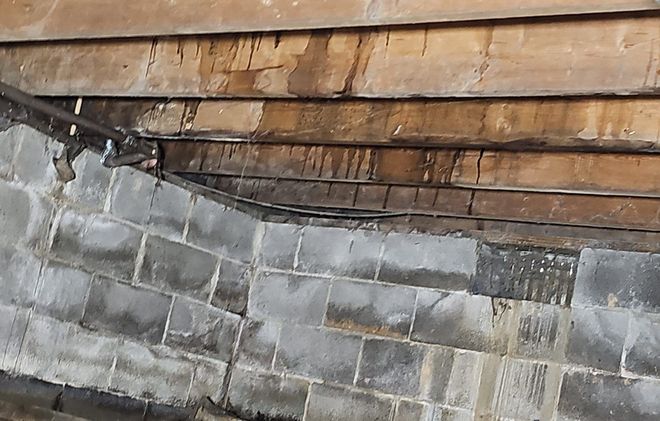 A view looking up at a concrete block wall meeting dark, weathered wooden roof decking showing signs of water damage.