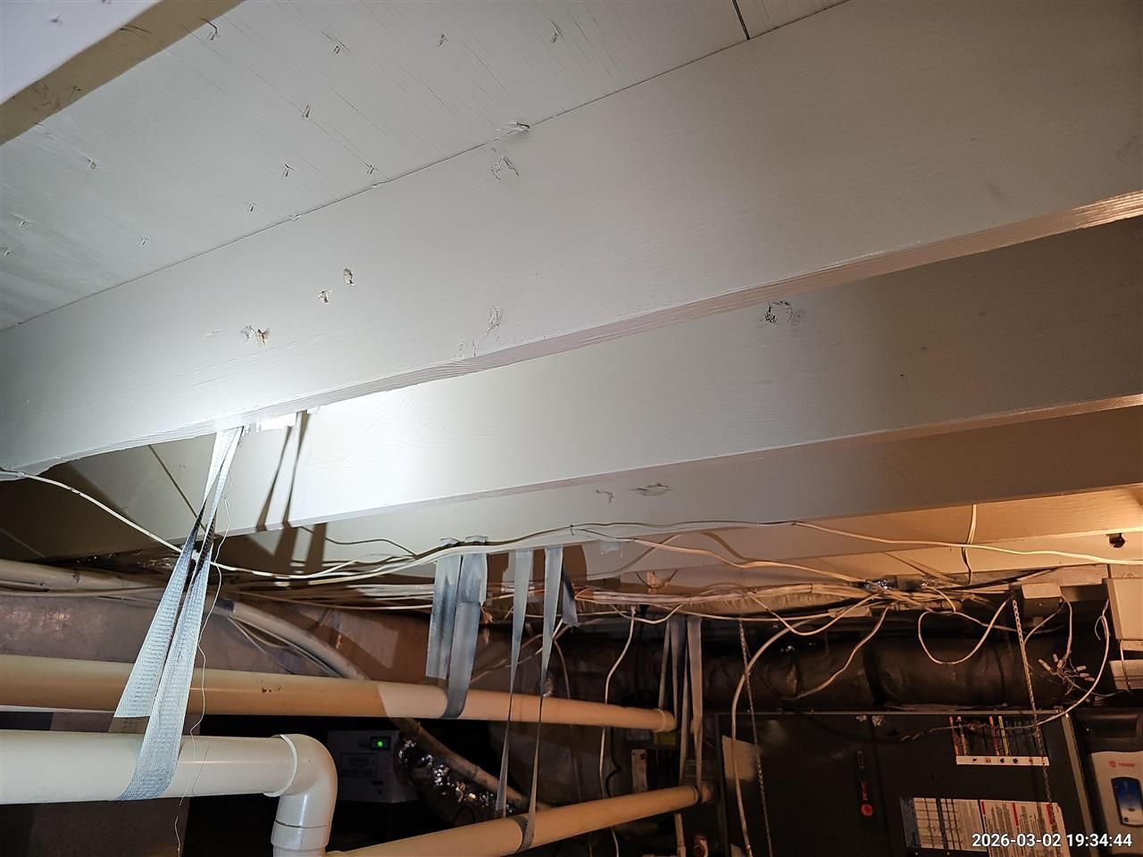 Ductwork suspended by tape straps from a ceiling in an unfinished basement or crawl space.