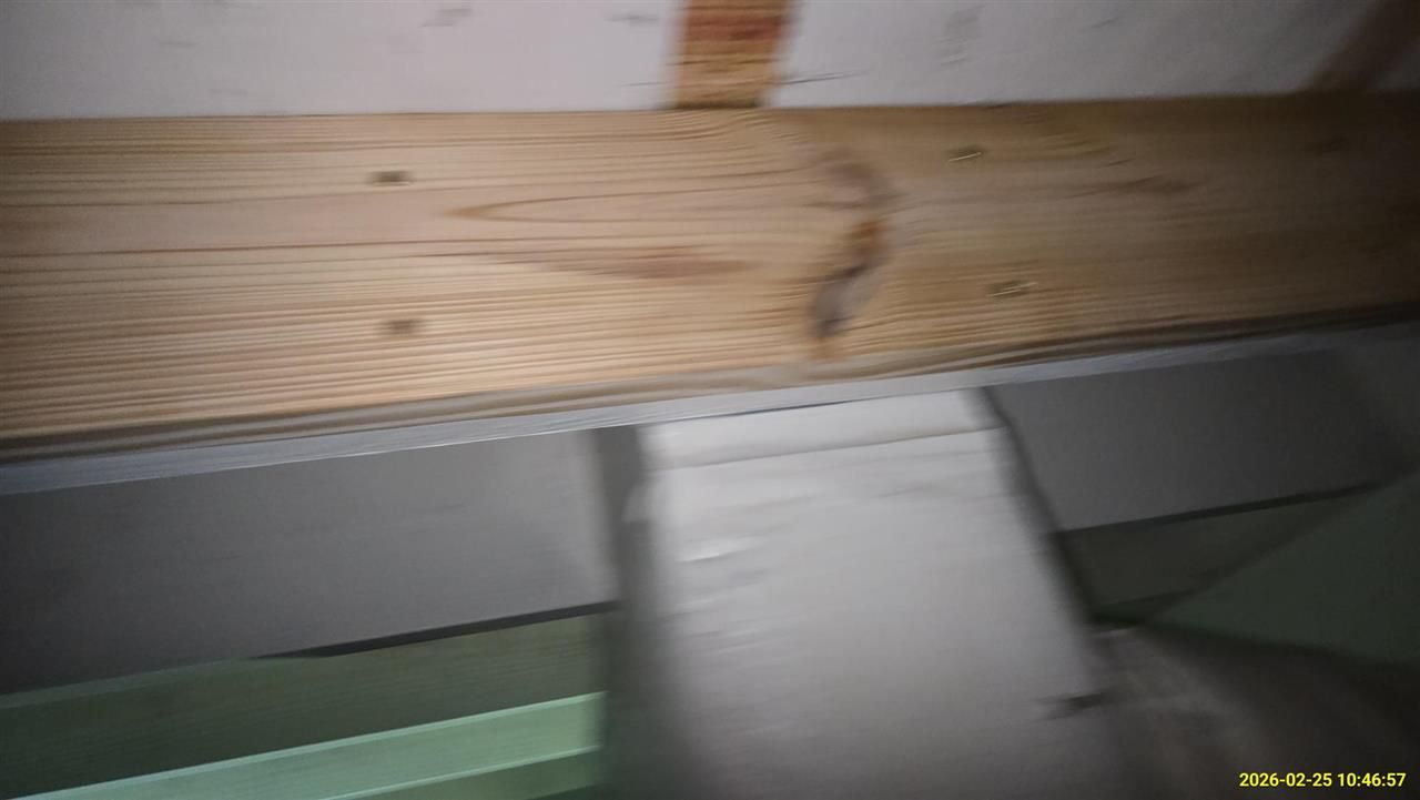 A horizontal wooden beam mounted above a grey wall section, featuring a perforated metal trim along the bottom edge.