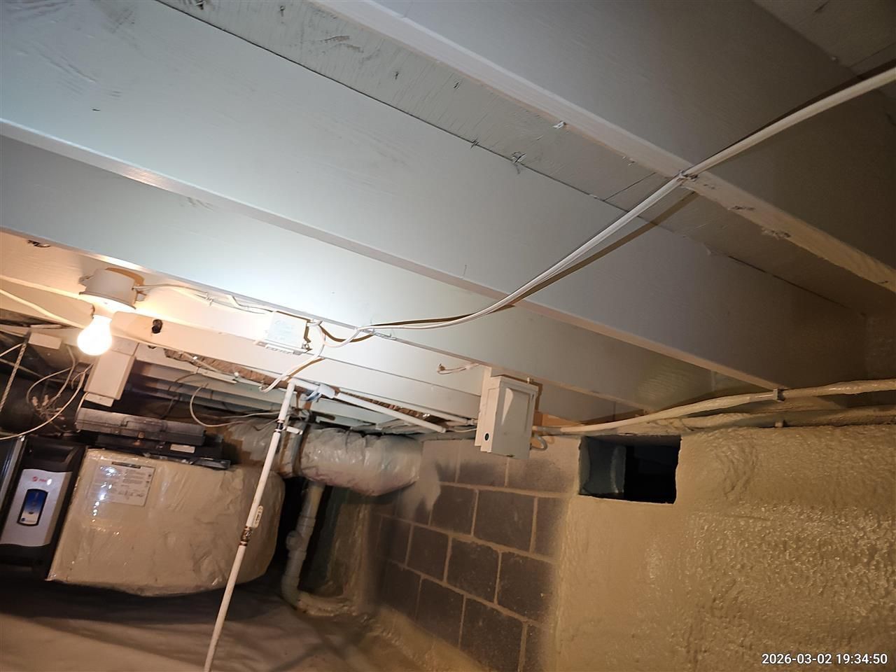 Exposed ceiling joists in a crawl space with visible wiring, insulation, and a water heater tank in the background.