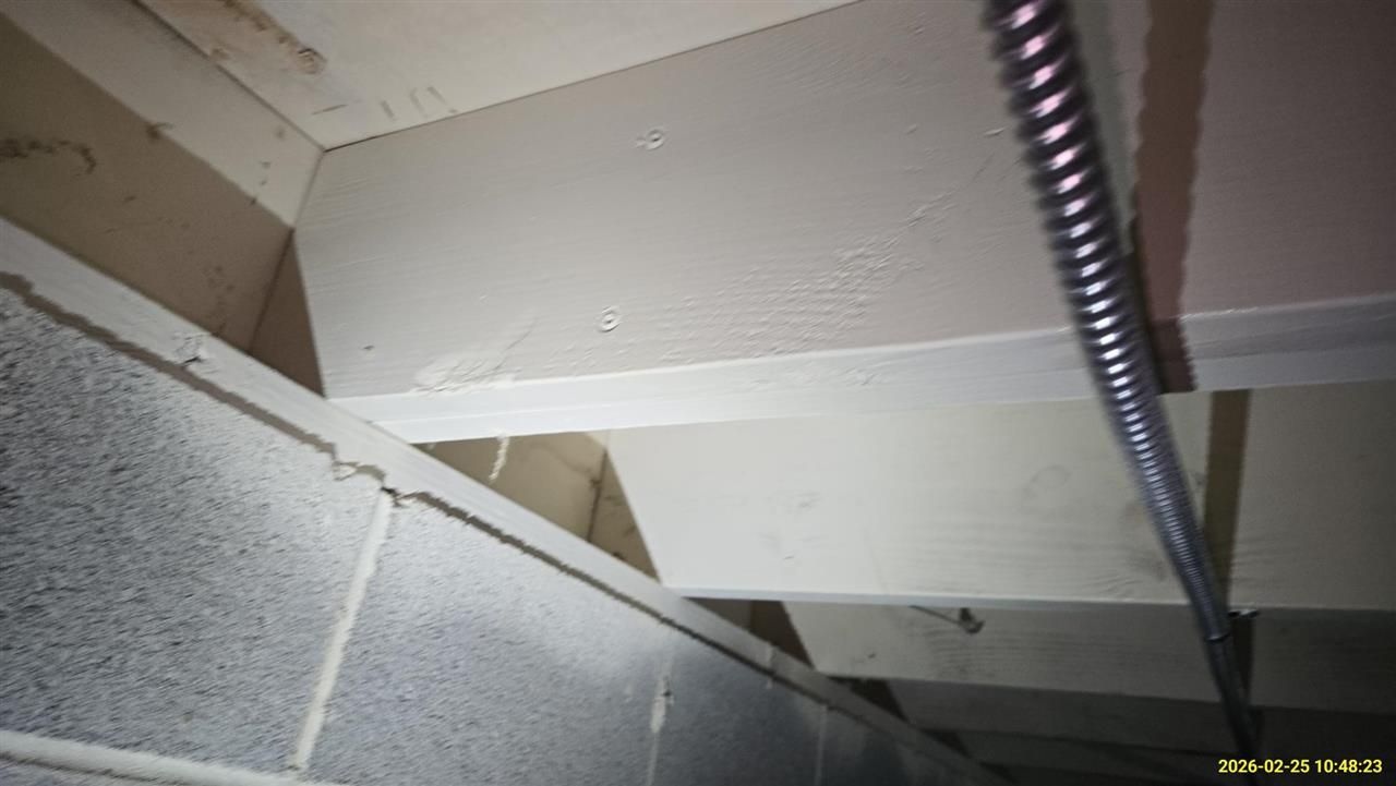 Close-up view of wooden joists resting on a concrete block wall in an unfinished basement with metal conduit overhead.