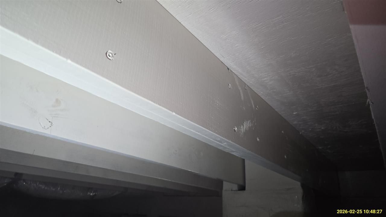 A close-up view of an indoor drywall ceiling with visible screws, seams, and textured surface in dim lighting.