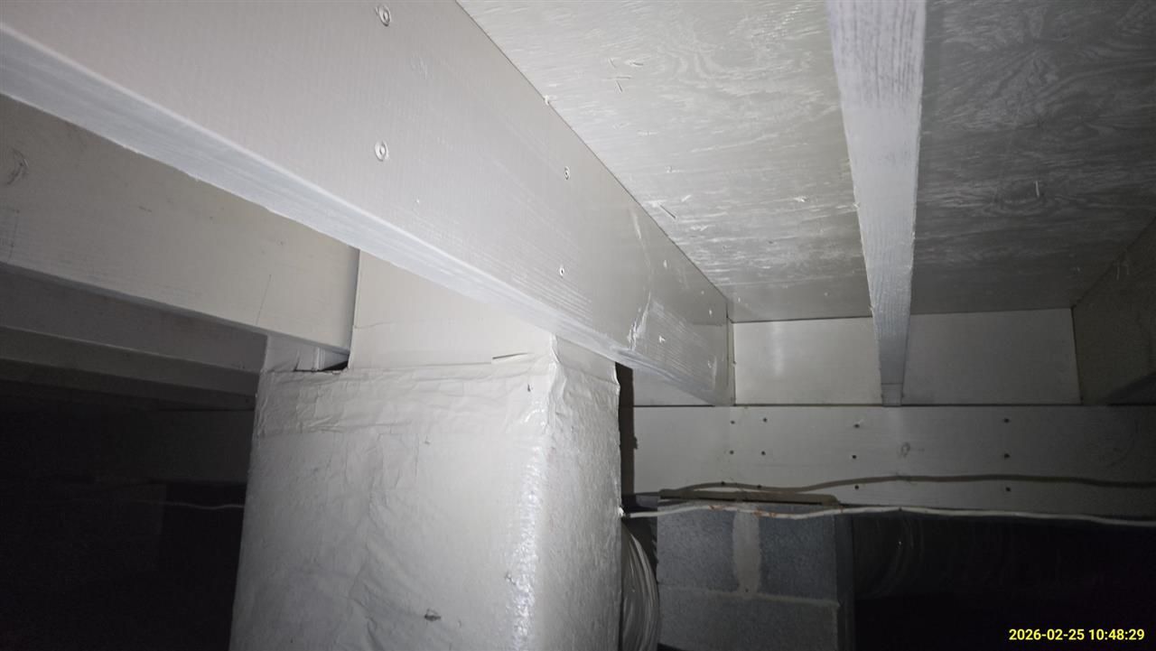 A close-up view of painted white support beams and columns in a crawl space, with wires running along the foundation.