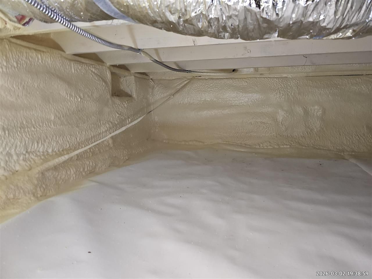 A crawlspace featuring white foam-insulated foundation walls and a white vapor barrier covering the ground floor.