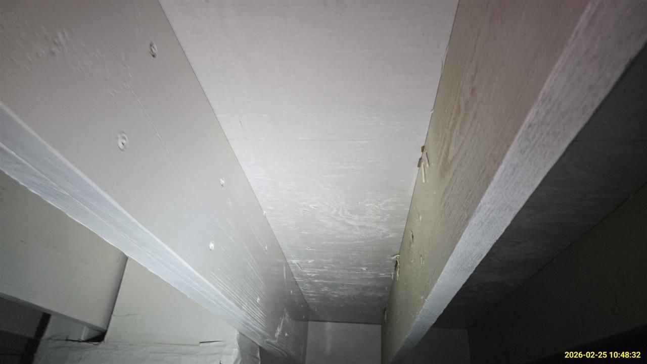 A low-angle view of white-painted ceiling joists and subflooring in a crawlspace or basement.