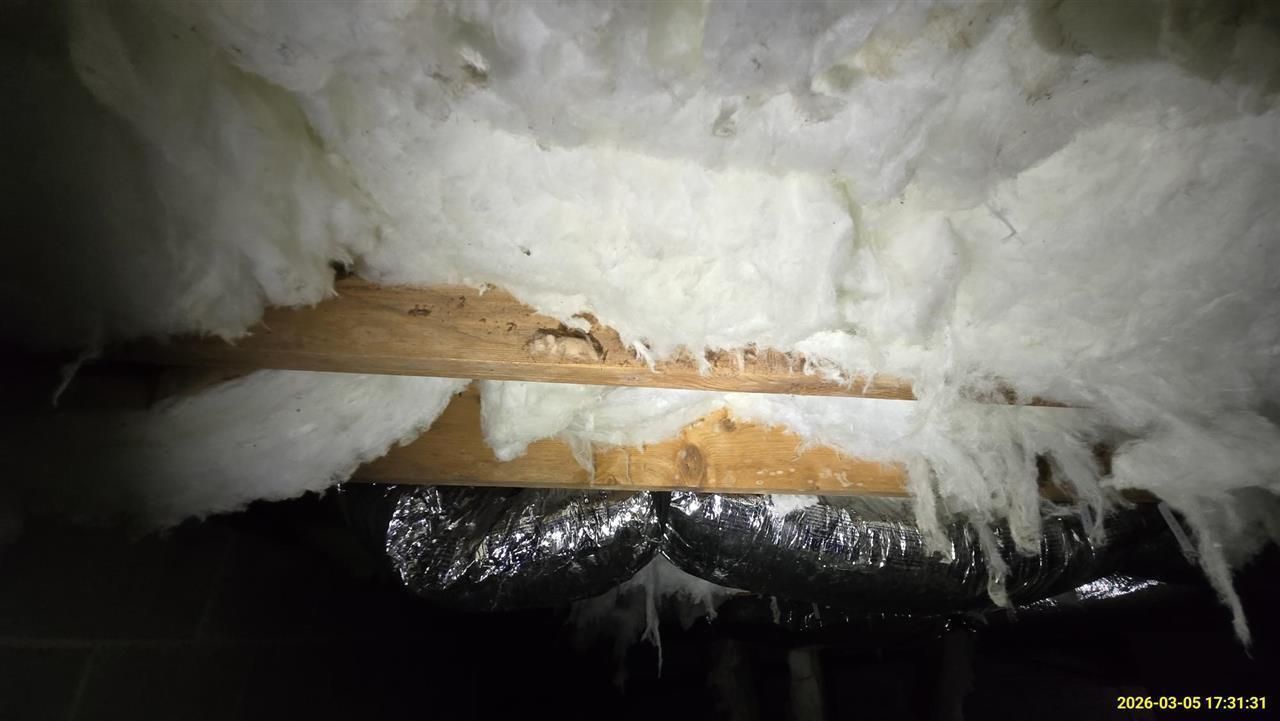 Fiberglass insulation batts installed in an attic, partially obscuring wooden structural framing and ductwork.