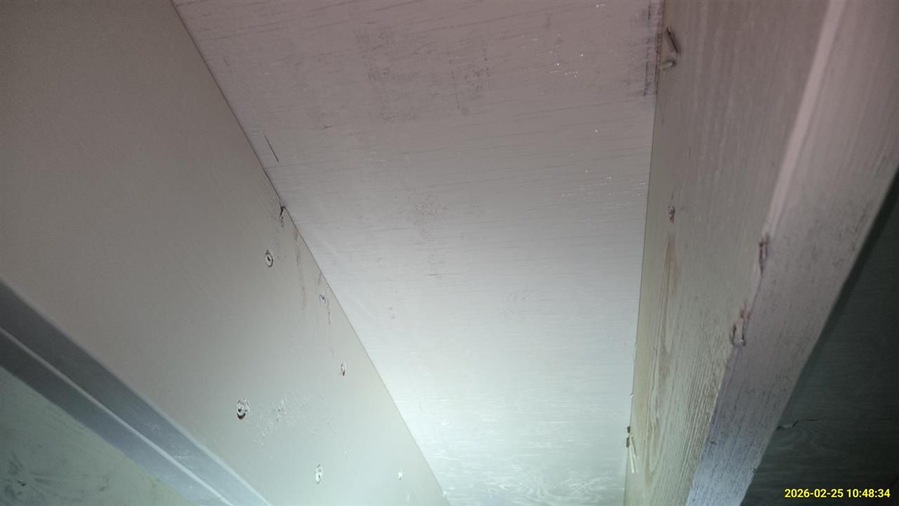 A white ceiling surface framed by two painted wooden beams, viewed from below in a dimly lit space.