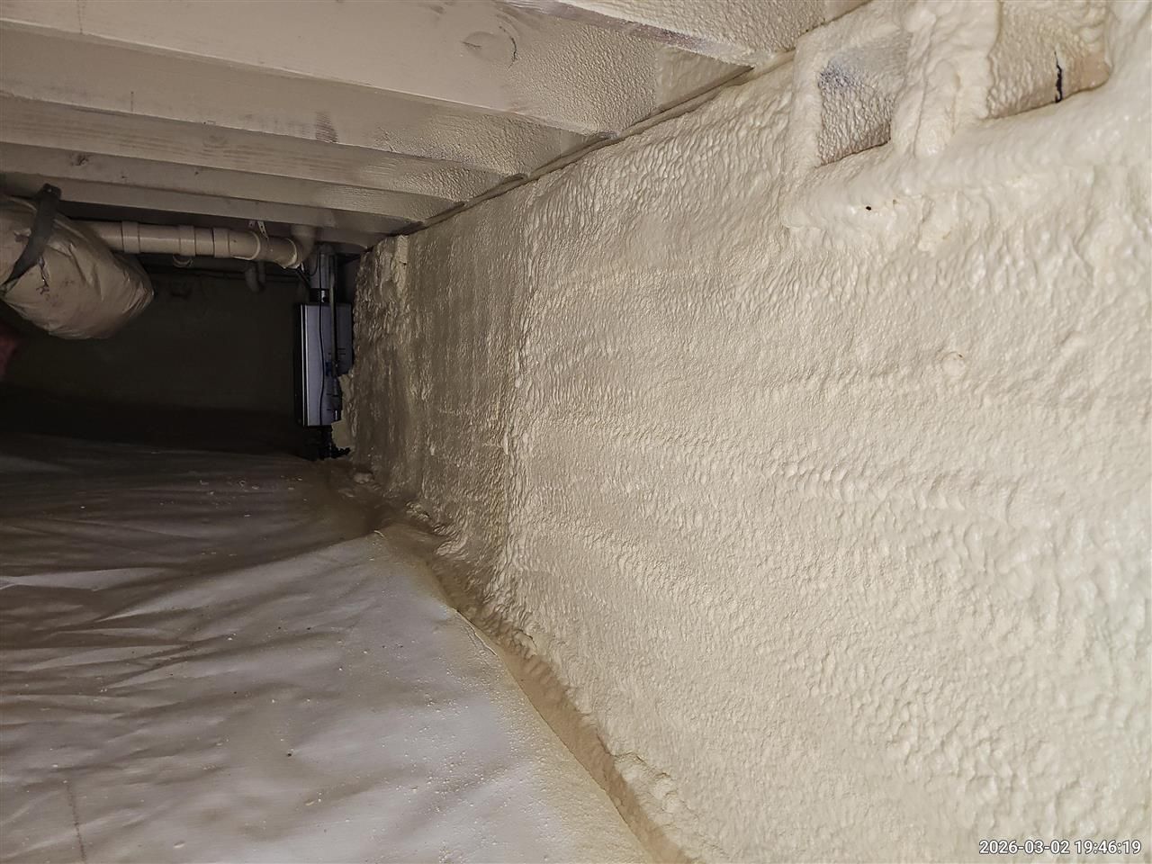 Crawl space with white vapor barrier flooring and spray foam insulation applied to the foundation walls and subfloor.