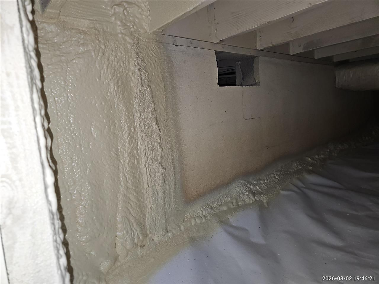 A crawl space with spray foam insulation on the foundation walls and a white vapor barrier on the floor.