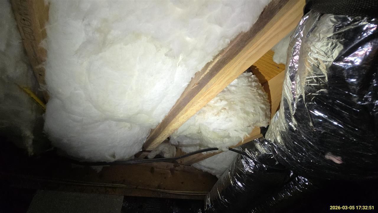 Attic view showing wooden rafters, white fiberglass insulation batting, and black insulated ducting.