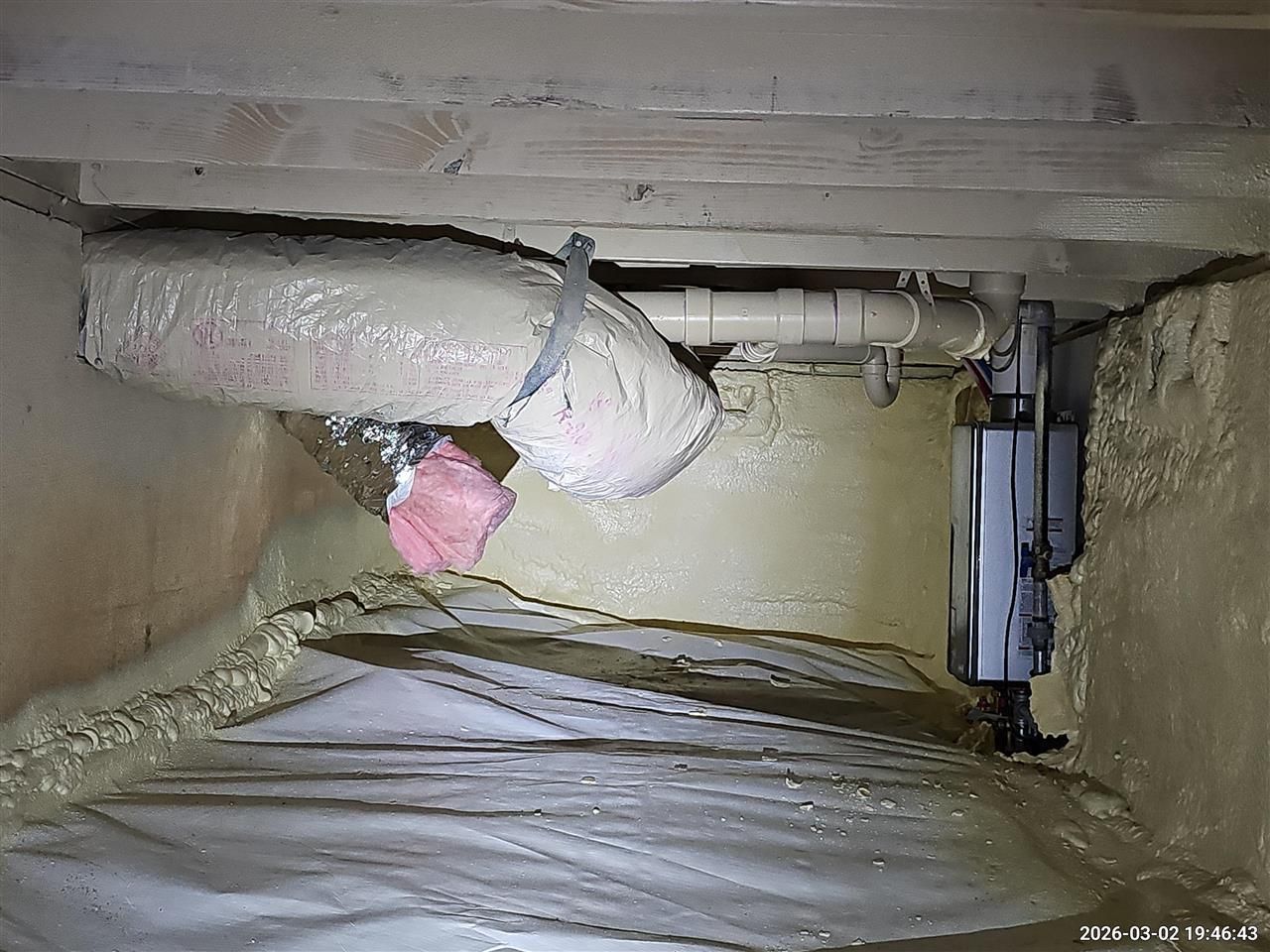 Crawl space with spray-foamed walls, insulated ductwork, plumbing pipes, and a white vapor barrier on the floor.