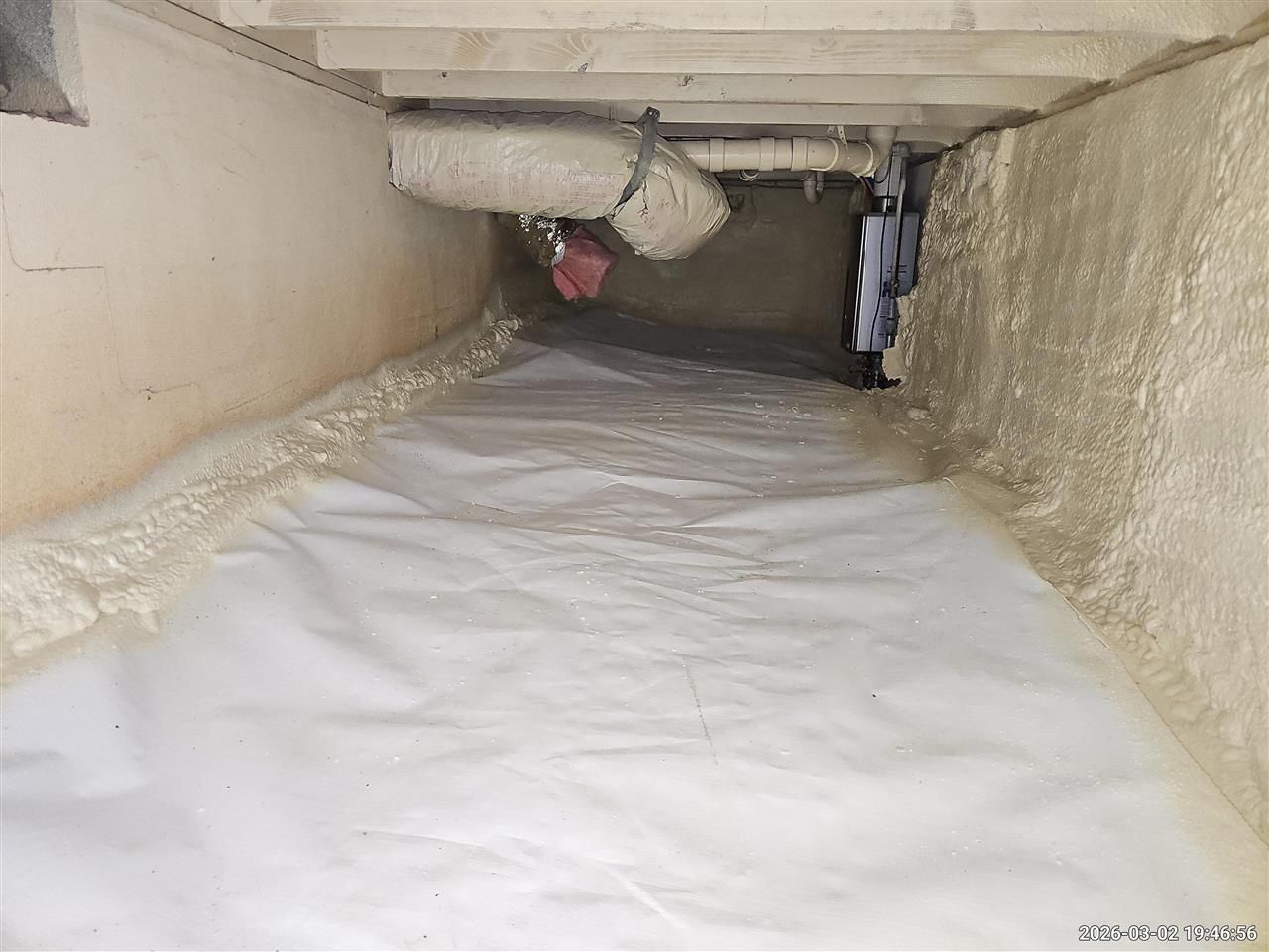 A crawl space with white plastic vapor barrier flooring and spray-foam insulation on the concrete foundation walls.