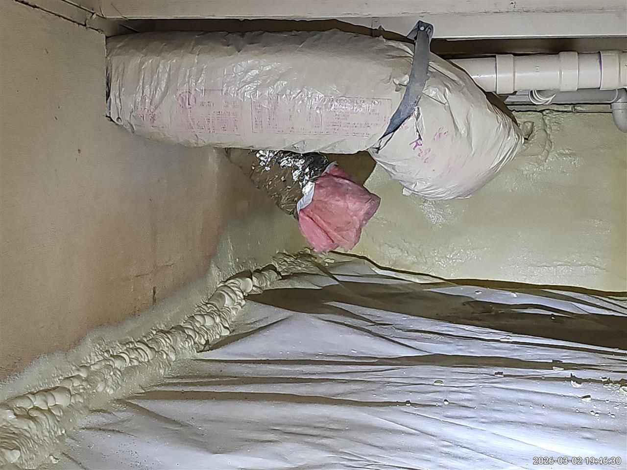 Insulated HVAC ductwork and white vapor barrier installed in a dark crawl space.