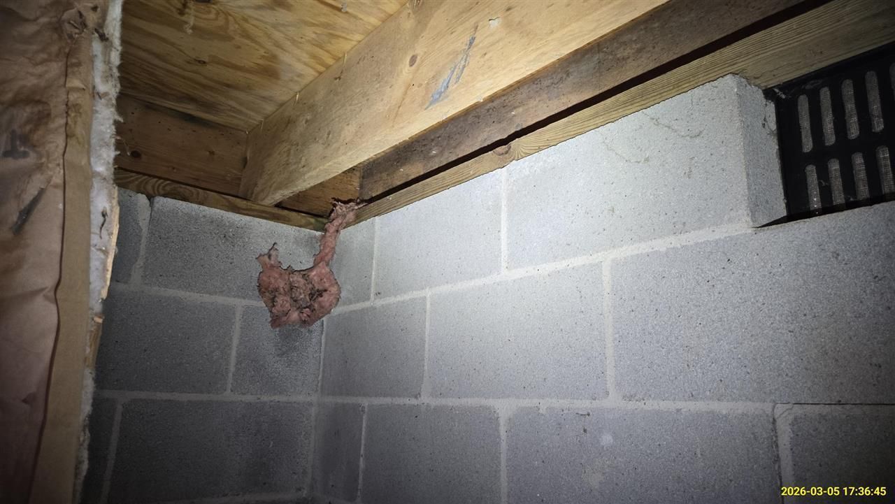 A crawl space foundation wall shows exposed fiberglass insulation hanging from the wooden rim joist.