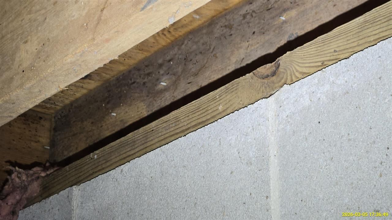 A wood joist sits atop a gray concrete block foundation wall, showing a large gap between the wood and the wall.