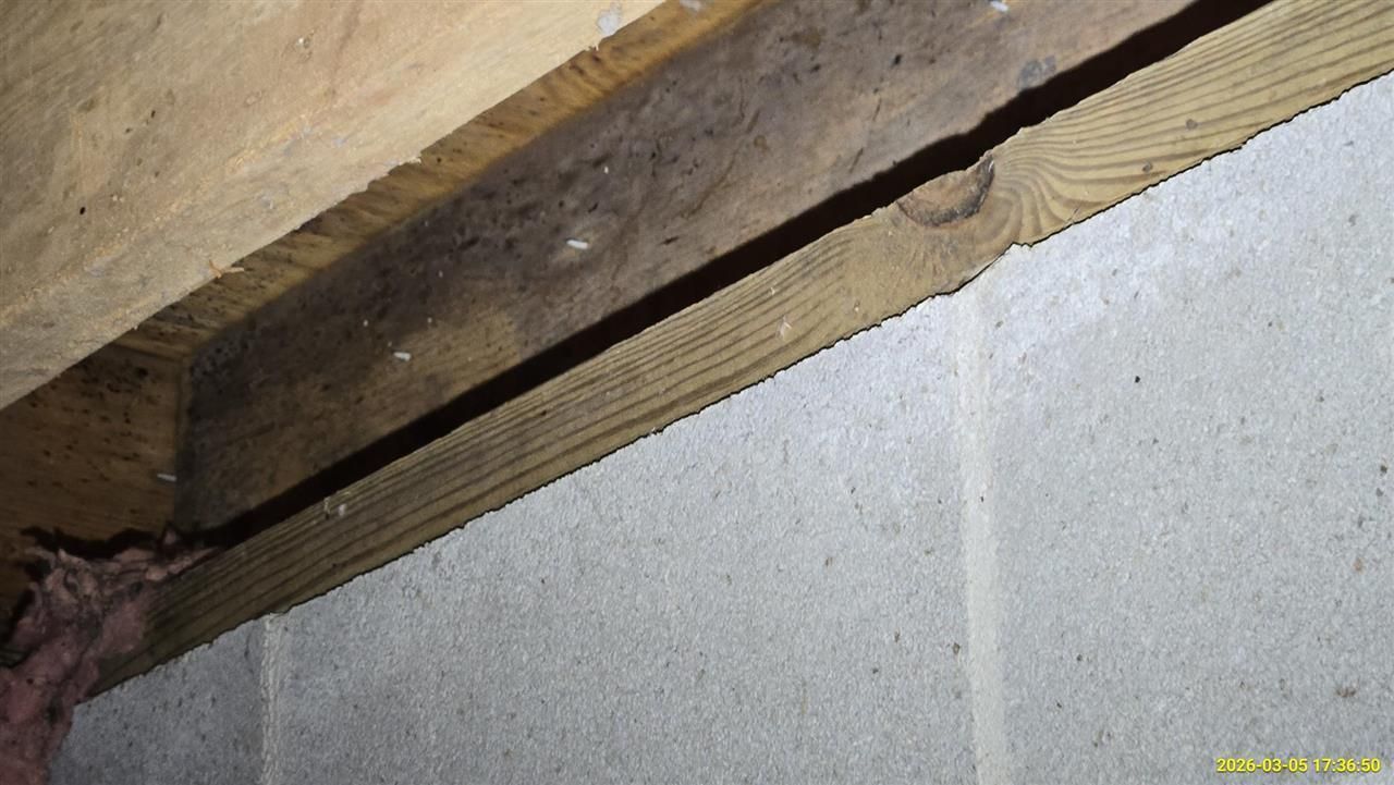 A wooden beam sits atop a concrete block wall with a visible gap between them.