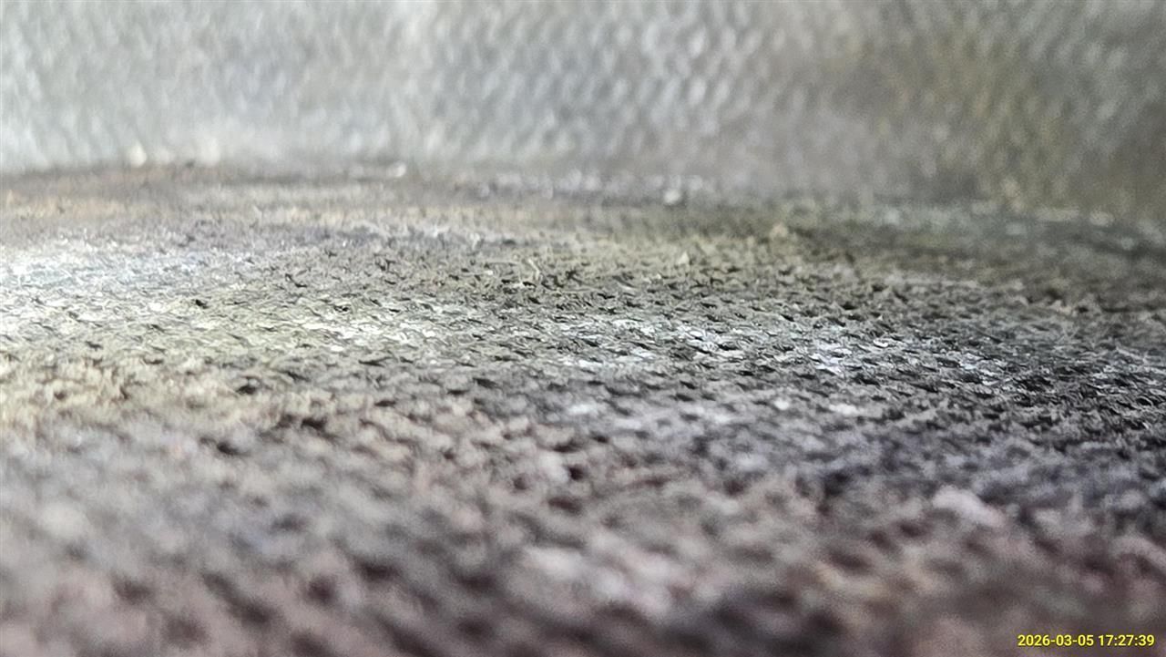 A close-up, angled view of a dark, textured fabric surface with a woven, coarse pattern.